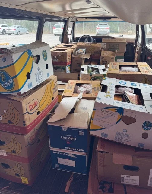 The back of a vehicle filled with frozen food and produce boxes, including banana boxes, some open and others closed.