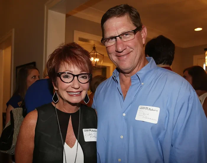 Two people smiling at an indoor social event, both wearing glasses and name tags.