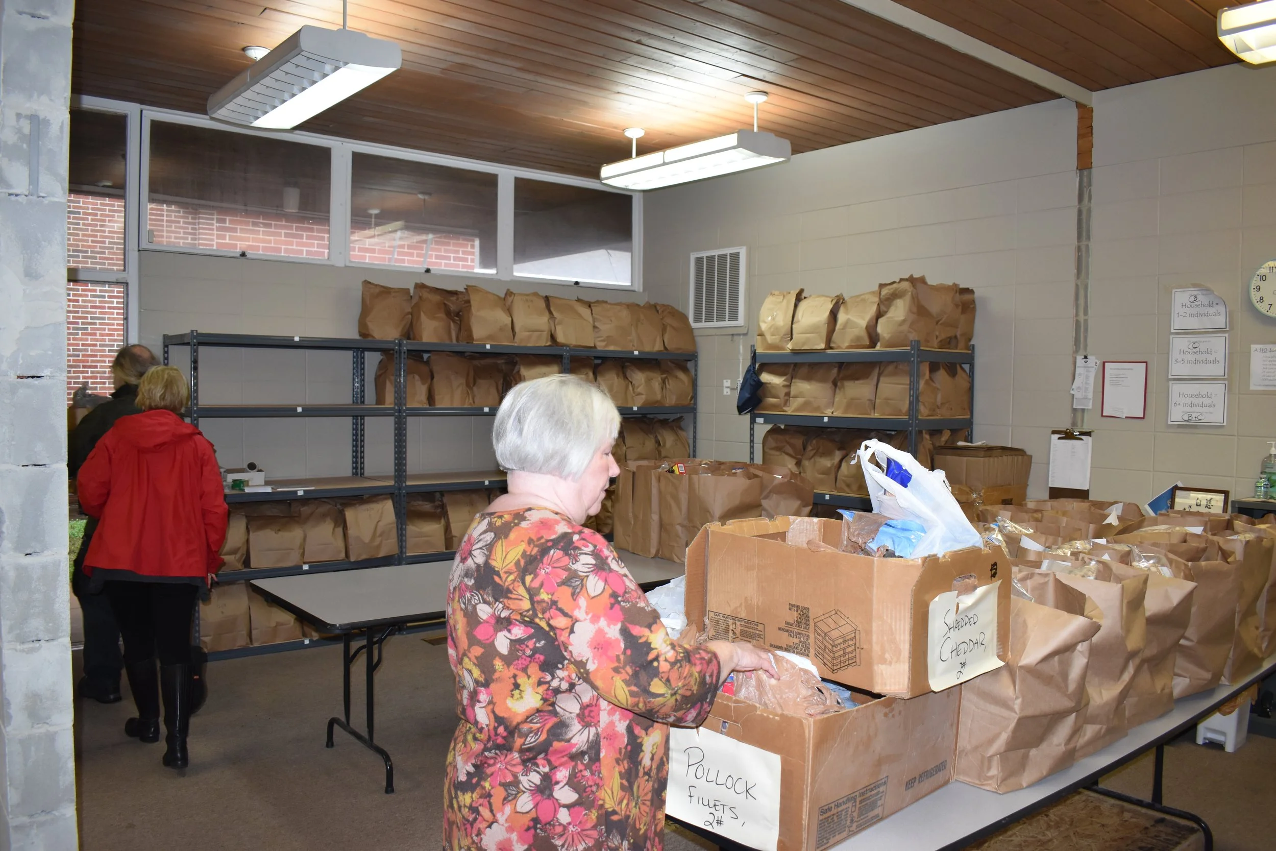 Women organizing food items in paper bags inside a community center storage room.