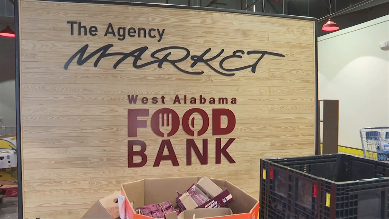 Sign for The Agency Market West Alabama Food Bank, with cardboard boxes and shopping carts in front.
