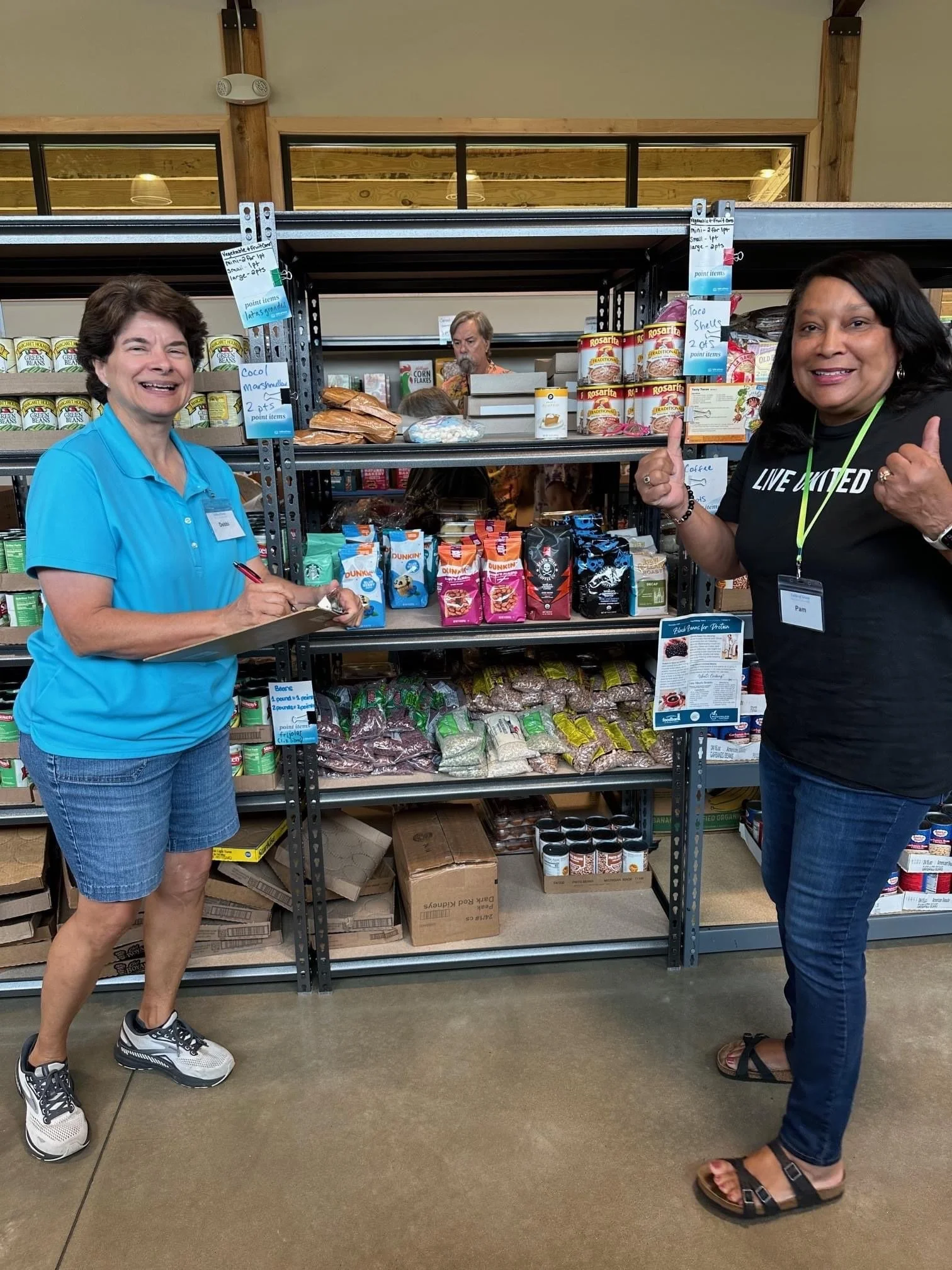 Two women standing in front of a grocery store shelf with various snacks and food items, smiling and giving thumbs up.