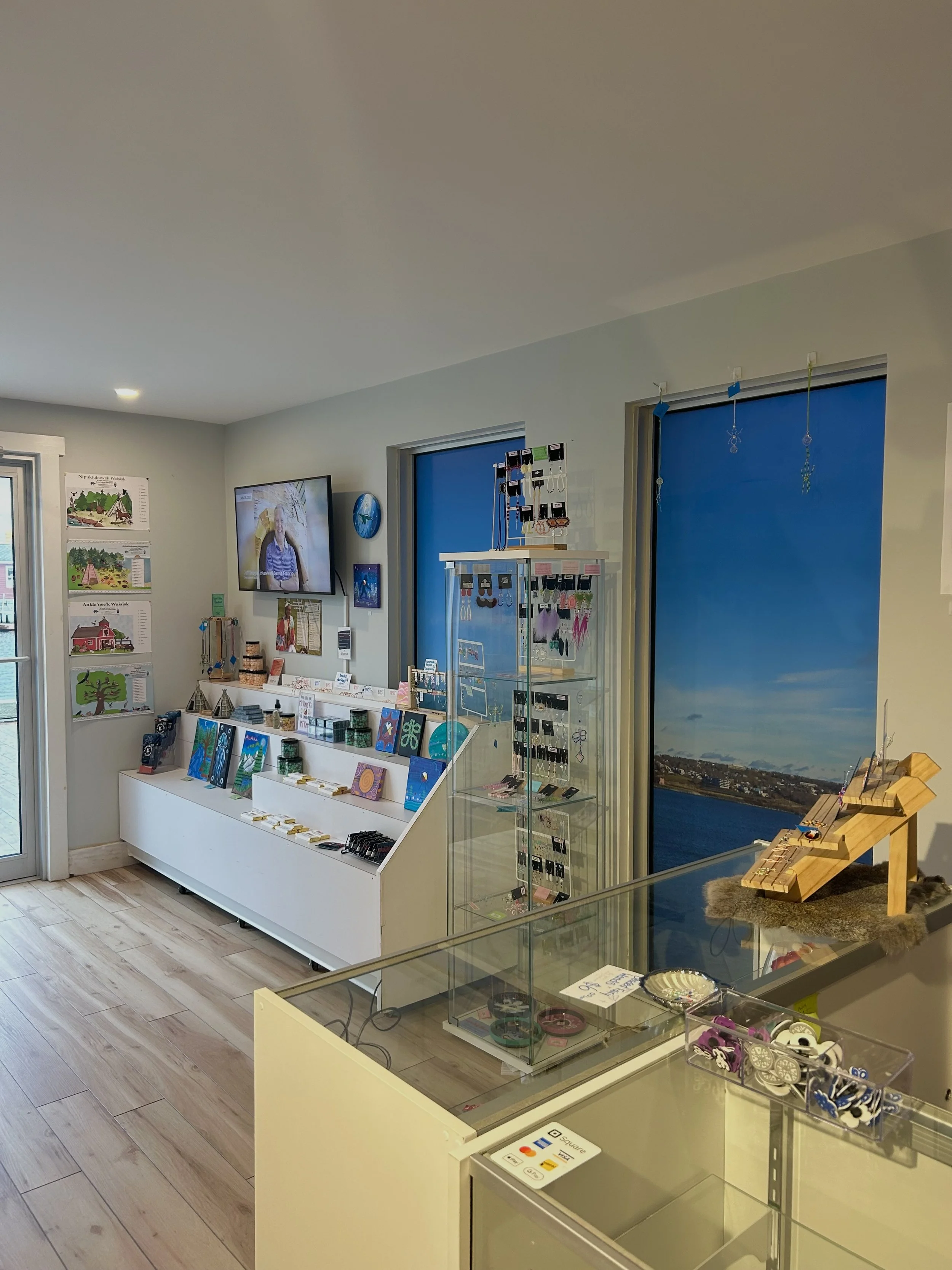 Interior of a gift shop with jewelry and artwork displays, a wall-mounted TV, and a mural of the seaside.