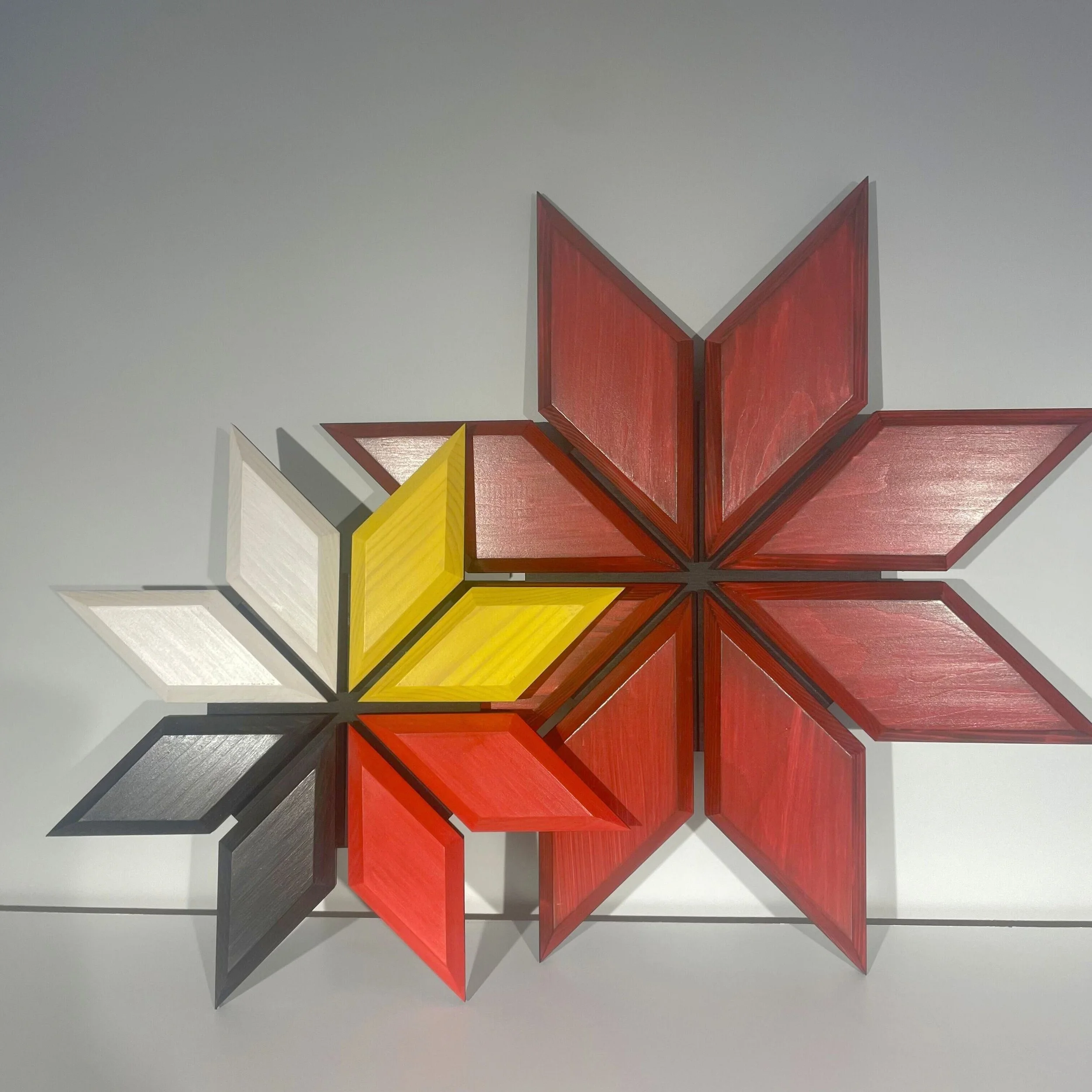 Colorful geometric wall art consisting of interlocking star-shaped panels in red, yellow, white, and black arranged in a floral pattern.