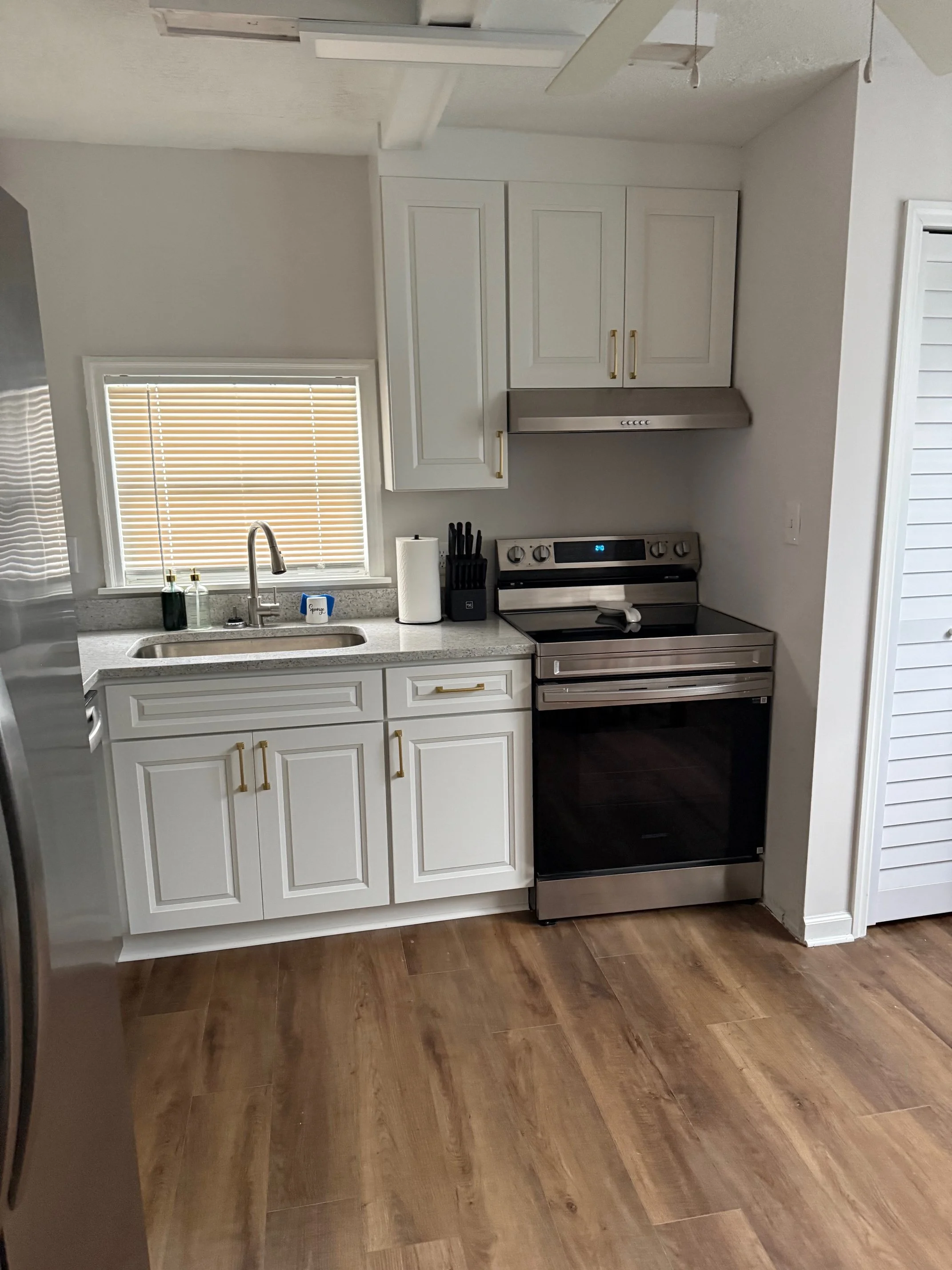 Kitchen with white cabinets, stainless steel stove, window with blinds, wood flooring.