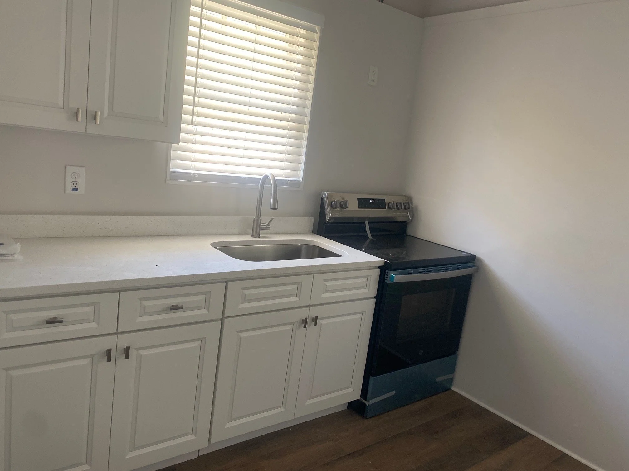 Modern kitchen with white cabinets, a stainless steel sink, a window with blinds, and a black stove/oven.