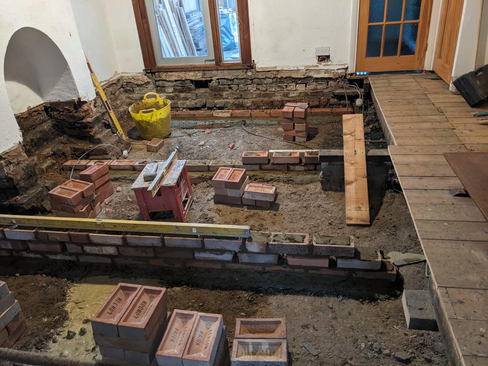 Room under renovation by K G Croft in north london with exposed brick walls, construction tools, and stored bricks.