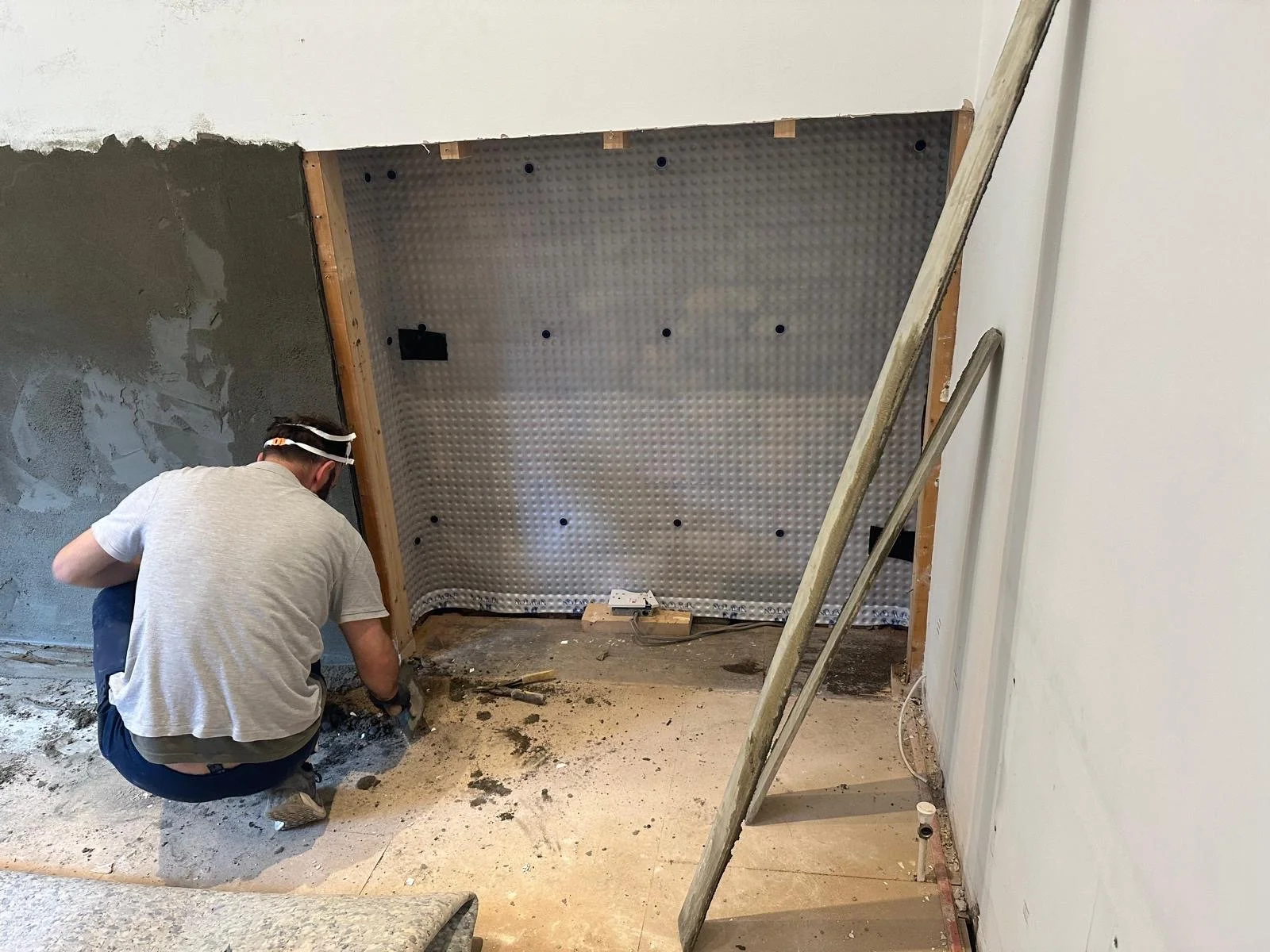 A person working on a home improvement project, installing or repairing a wall or ceiling with construction tools and materials visible.