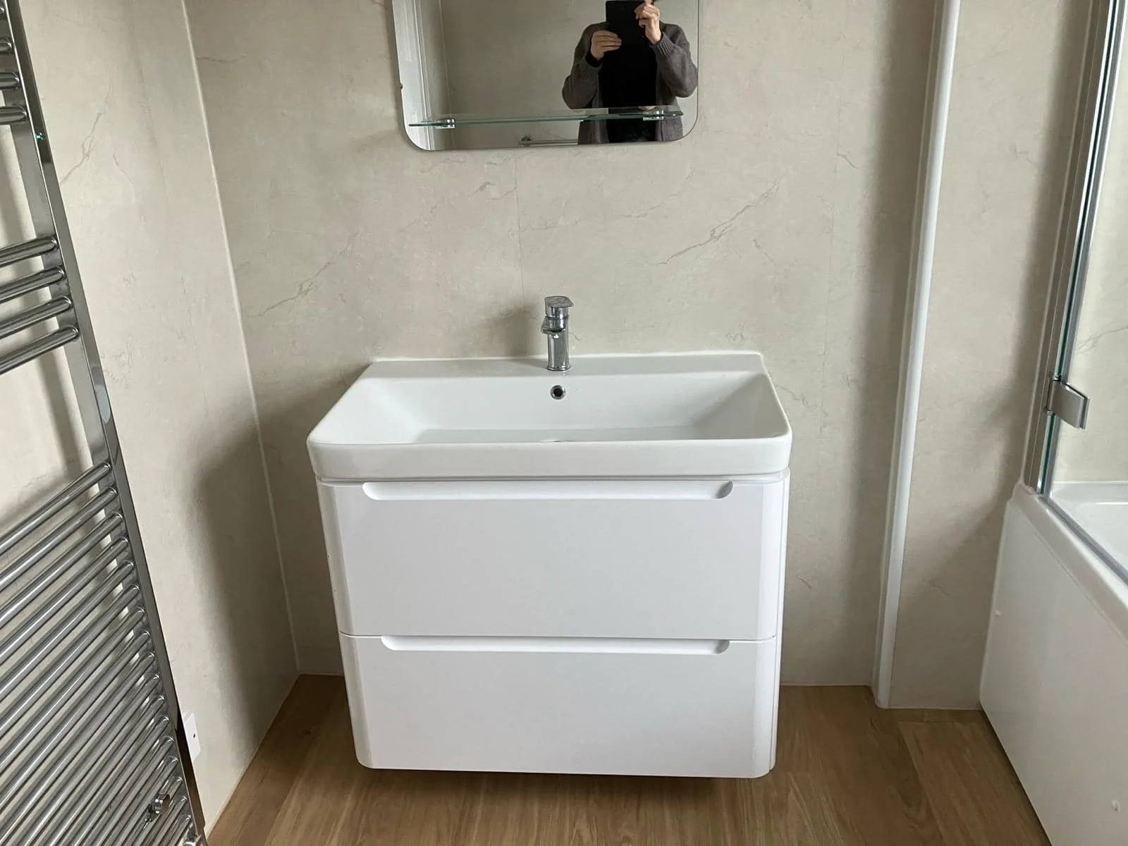 A white bathroom vanity with a sink, mirror above, and faucet, in a bathroom with beige walls and wooden floor.