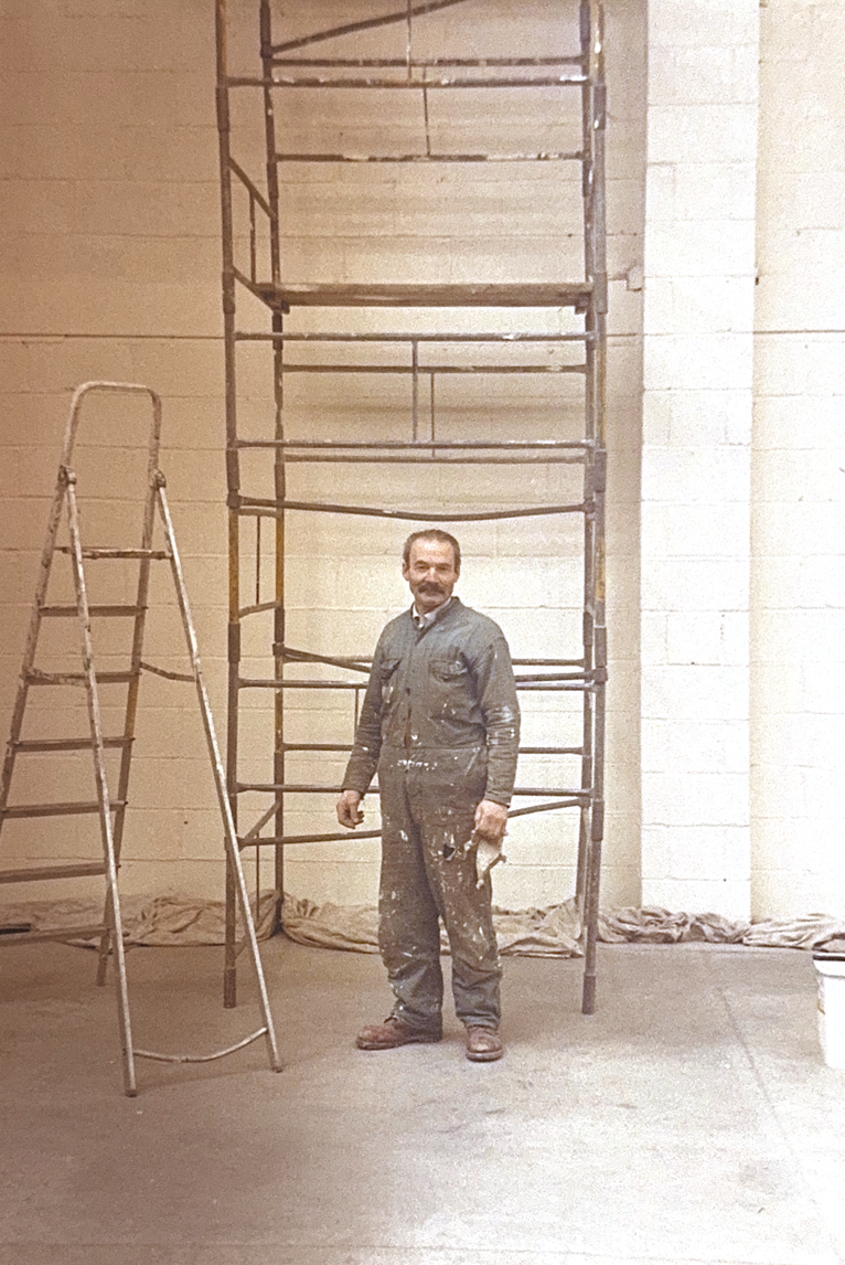 A man in work clothes standing next to a metal scaffolding and a ladder inside a building with unfinished walls. K G Croft archive images.
