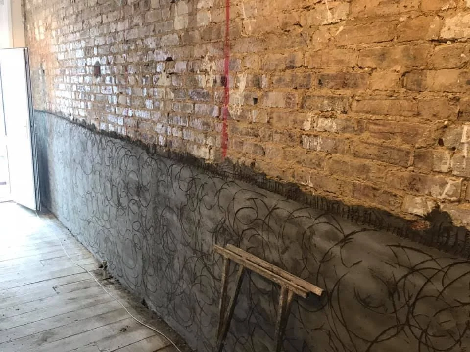 Brick wall with a lower section covered in concrete and rebar, with construction tools nearby.