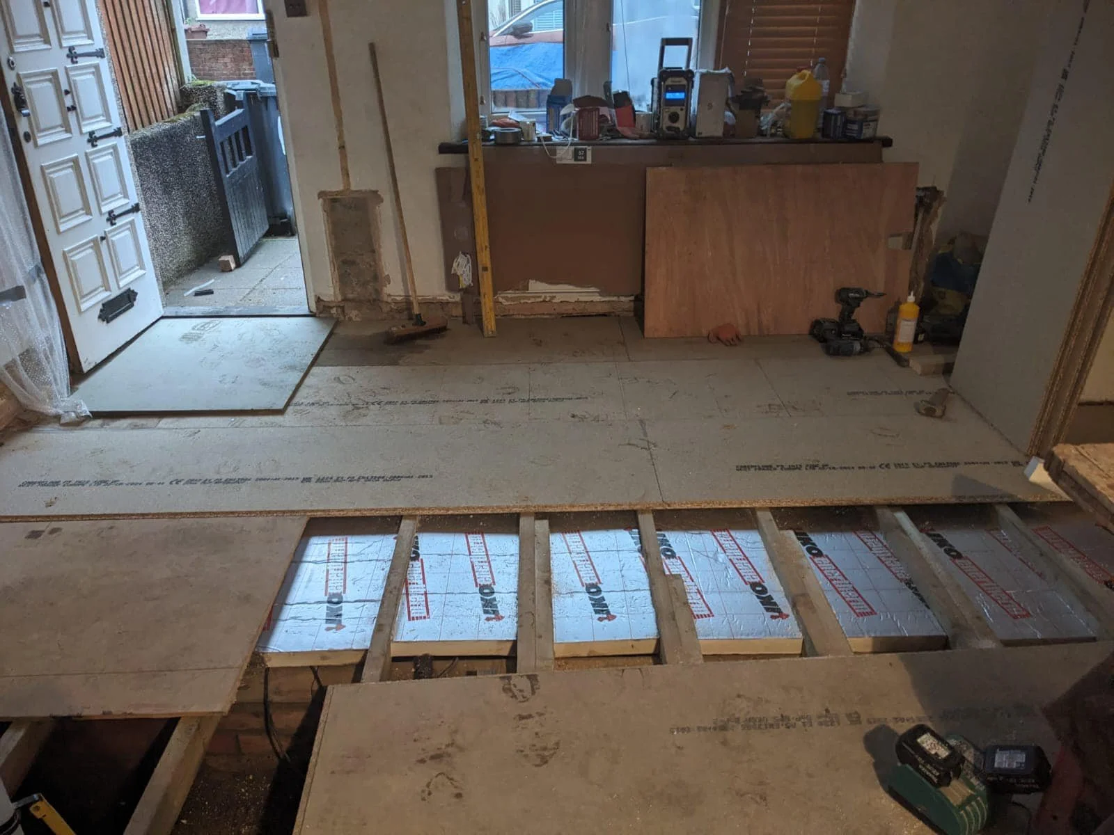 Interior in north london of a room under renovation with floor partially removed, exposing insulation and wood framing by K G Croft.