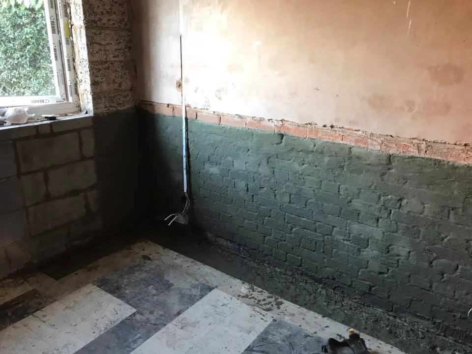 Empty room in north london under construction by K G Croft with brick walls, a window, and a checkered floor.