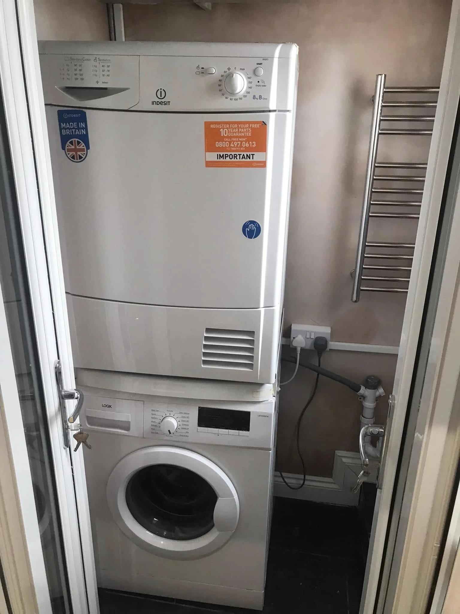 A stacked washer and dryer units in a laundry room, with a small space around them, and a heated towel rail on the wall to the right.