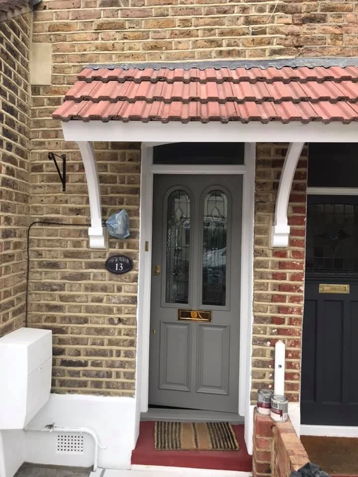 Front door with gray paint and decorative glass, brick house with small porch, red tiled roof, and a striped doormat.