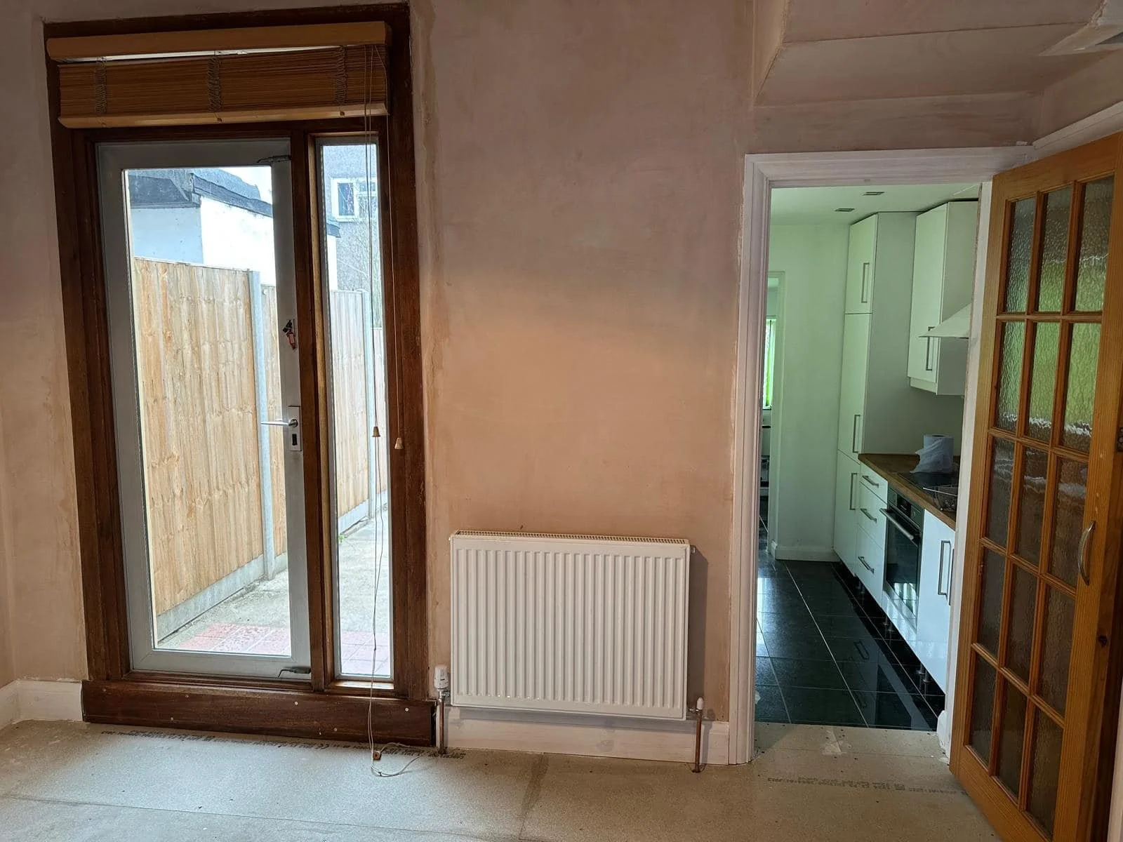 View of a living room leading to a kitchen, with a sliding glass door to an outdoor area, and a wooden door on the right side of the image.