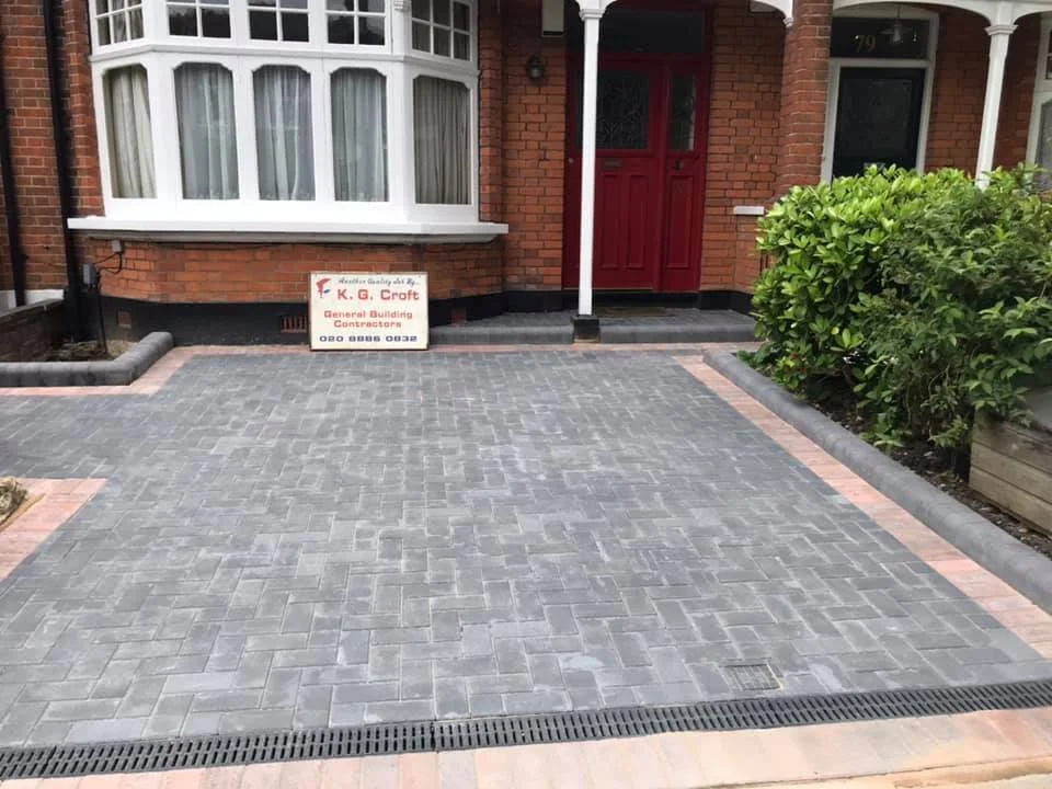 Freshly paved driveway in front of a red brick house with a red door, surrounded by green bushes by K G Croft in North London.