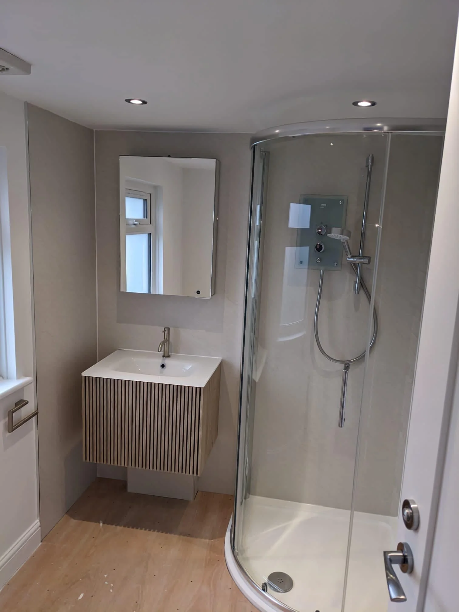 Small modern bathroom with a corner shower with glass door, a small vanity with a sink, a mirror above the sink, and a window.