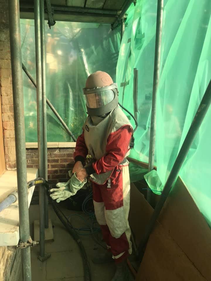 Worker in protective gear, including helmet and visor, preparing to use construction tools on a building's brick wall at a construction site. K G Croft damp works.
