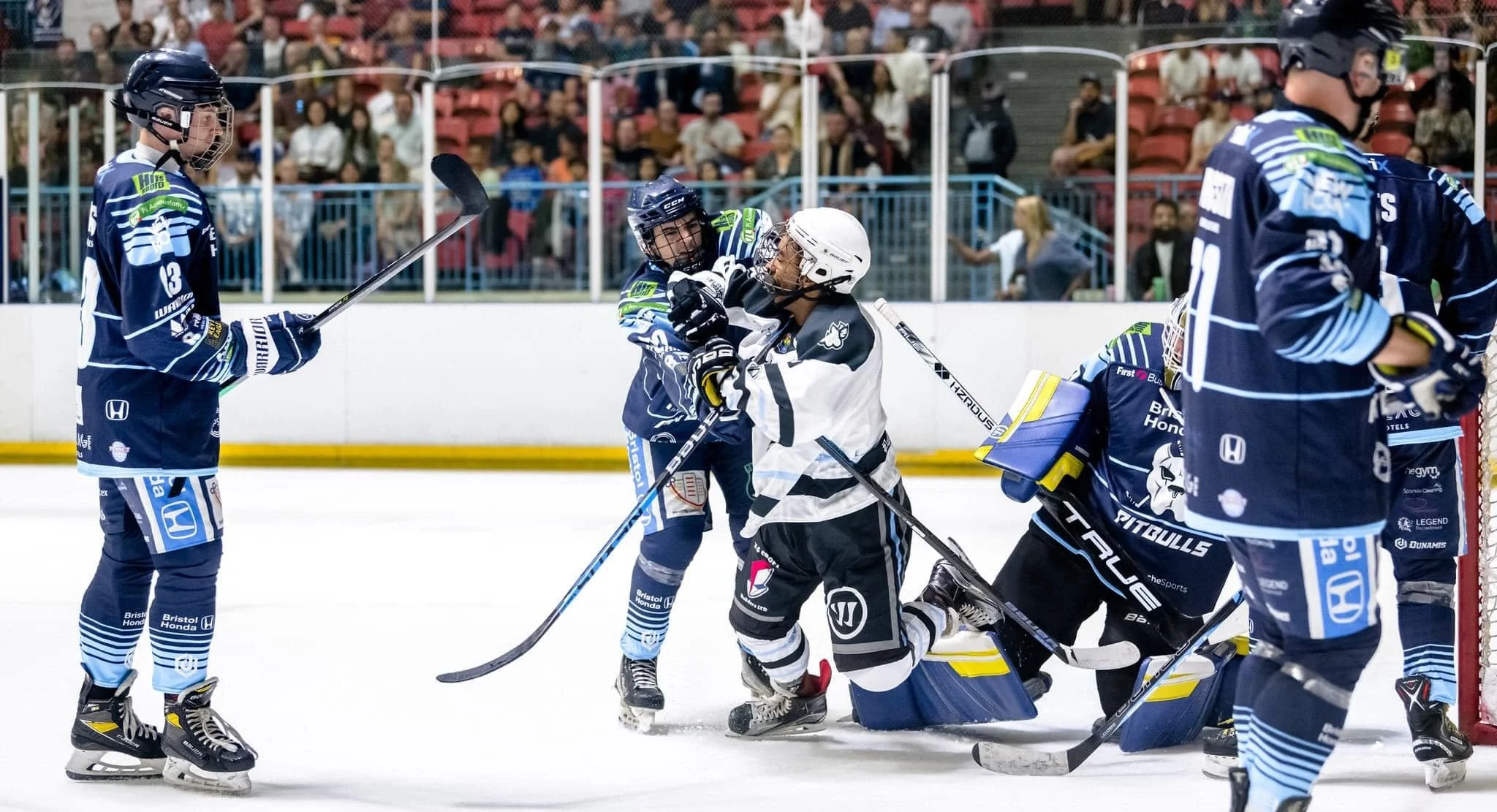 Harringay Huskies ice hockey players fighting on the ice rink during a game, with spectators watching in the background. Sponsored by K G Croft.