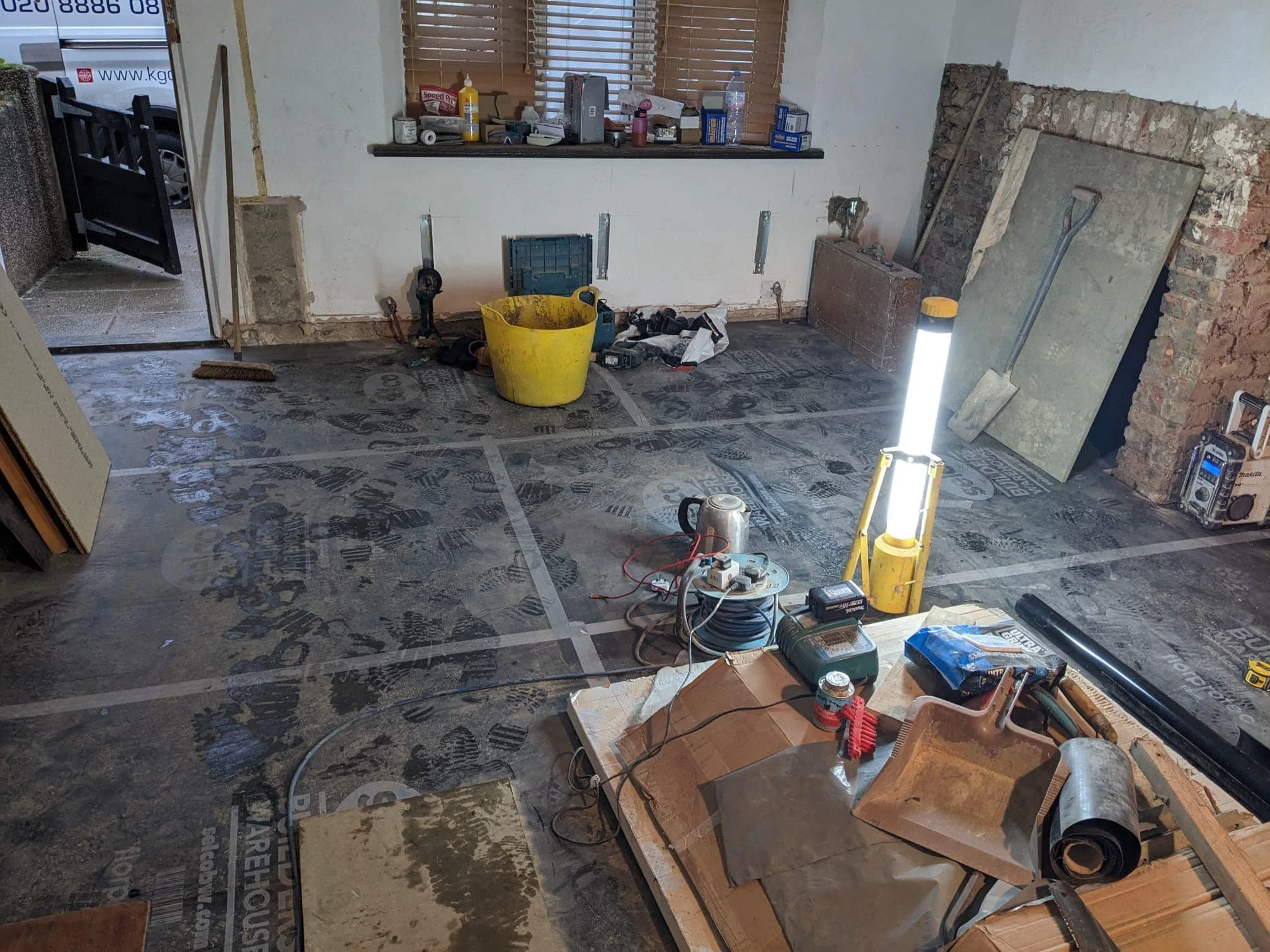 Interior of a room under renovation by K G Croft in north london with tools, construction materials, and a work light, in the process of flooring installation.