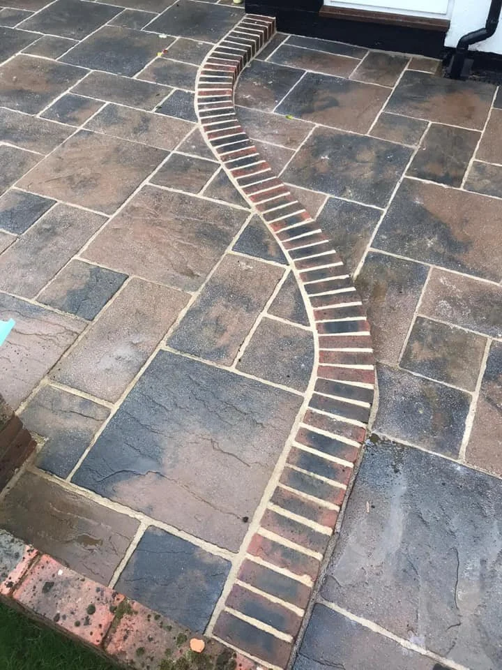 Decorative brick pathway on a stone patio, designed in a twisting, winding pattern.
