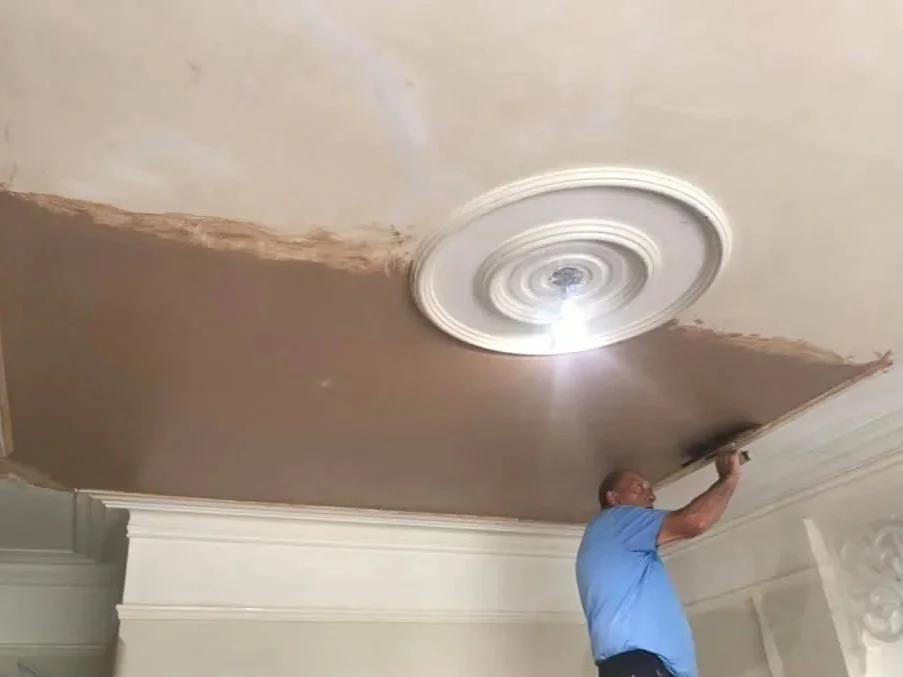 K G Croft employee is repairing a ceiling with a decorative ceiling medallion. The ceiling shows signs of damage or peeling paint nearby.