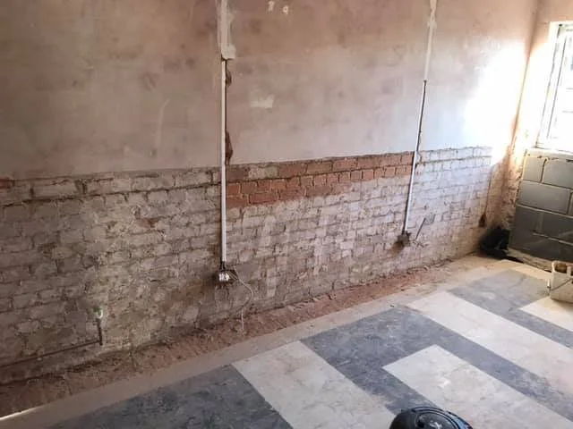 Interior wall under construction with exposed bricks and electrical conduit, and a partially finished floor.
