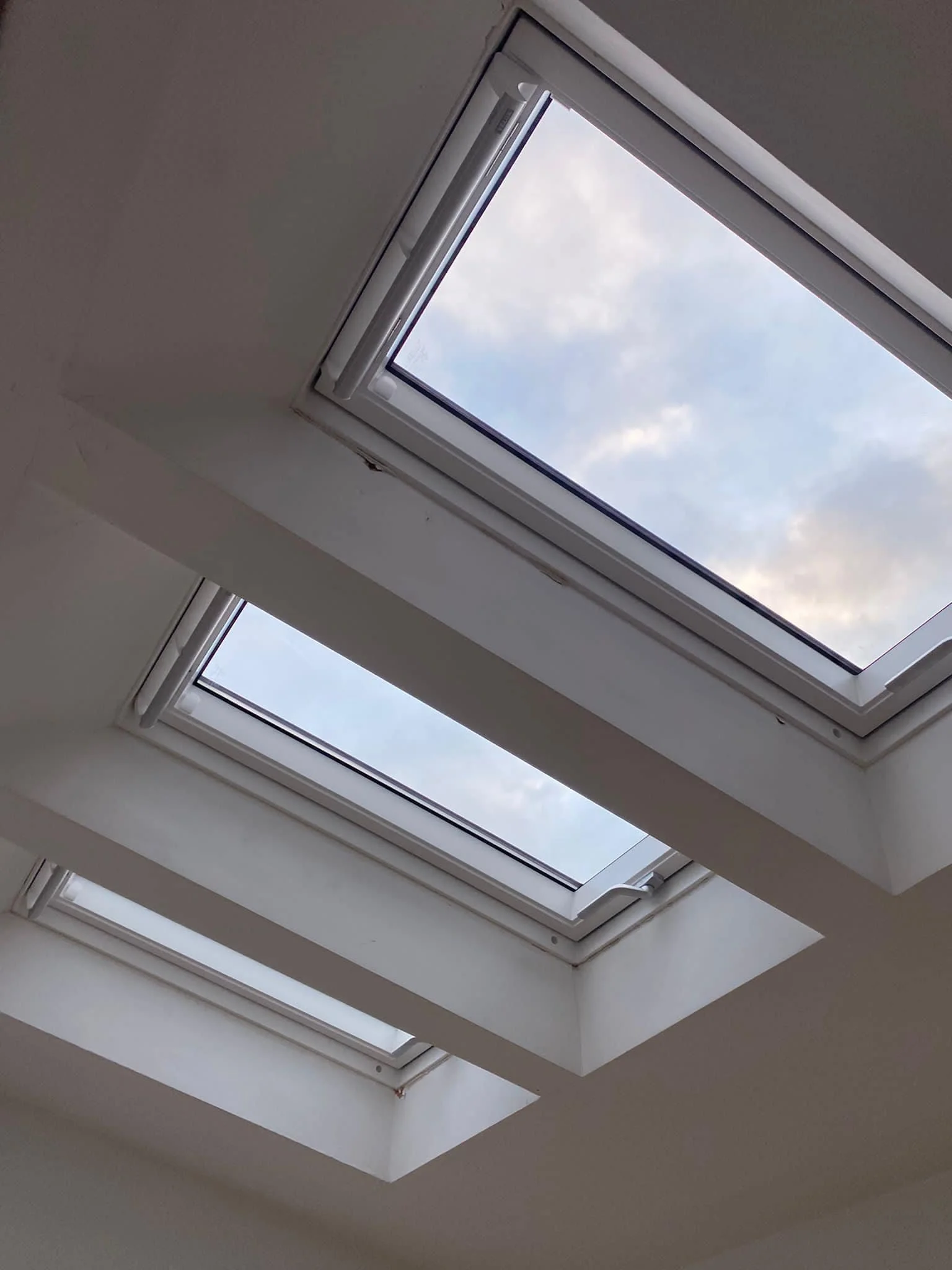 Three skylights on a white ceiling showing a partly cloudy sky.
