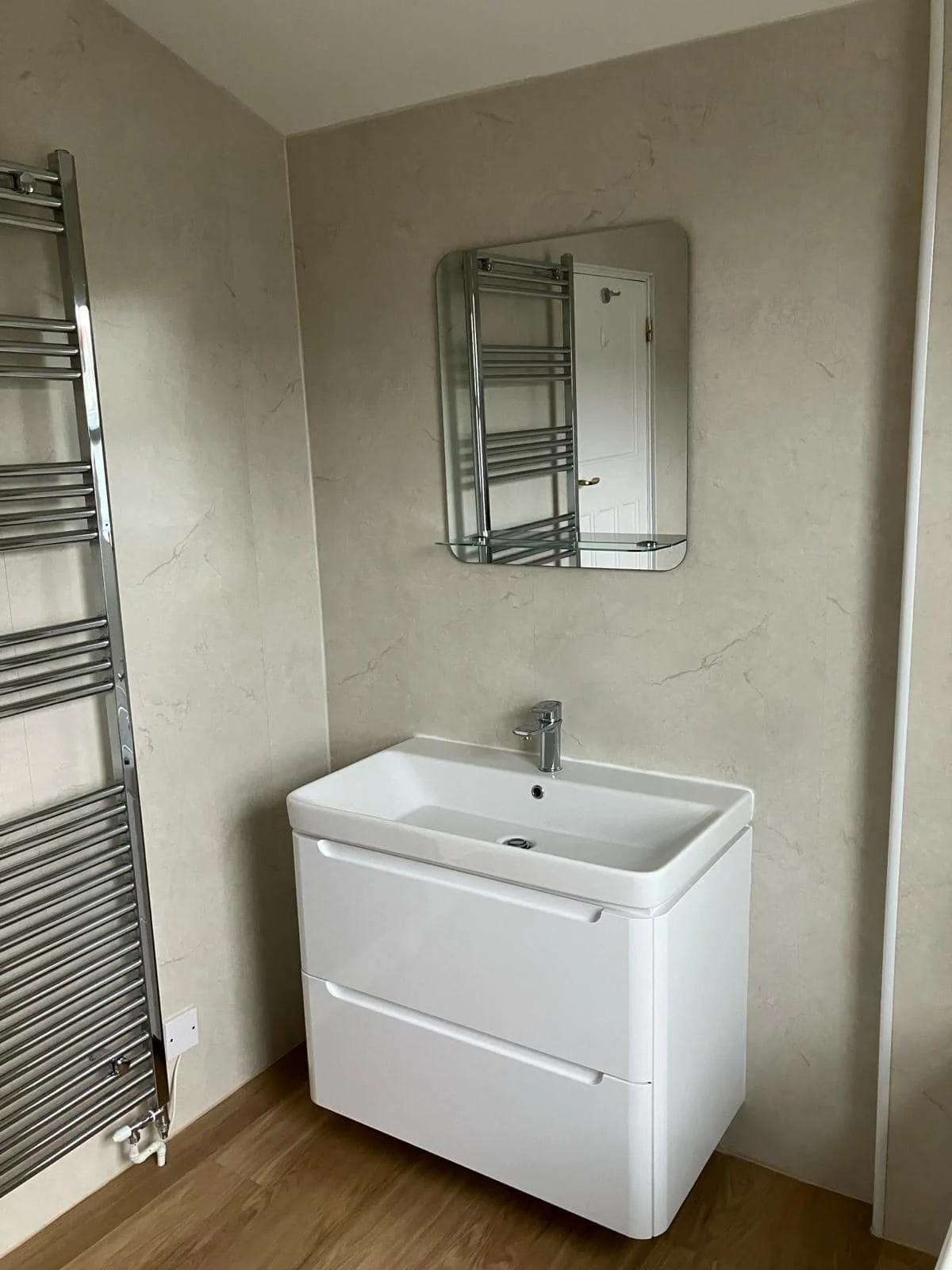 A bathroom sink with a mirror above and a towel heater on the left side.