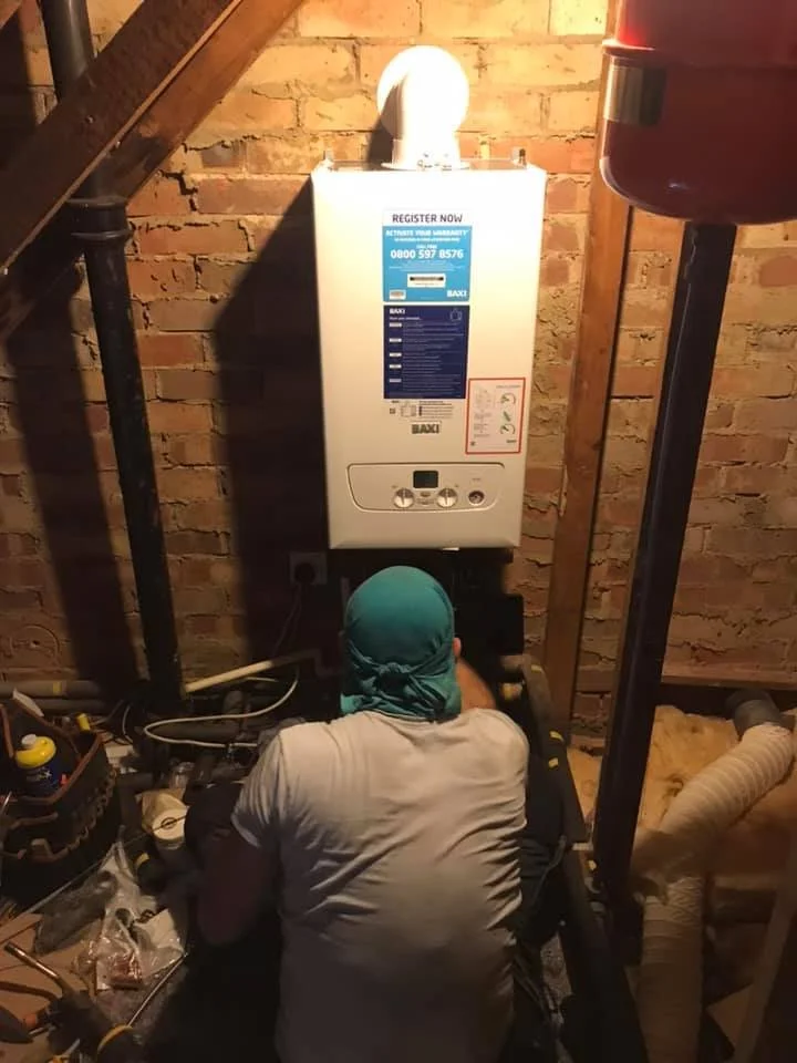 Person working on a boiler or water heater in a basement with exposed brick wall. K G Croft plumbing and heating works in north london.