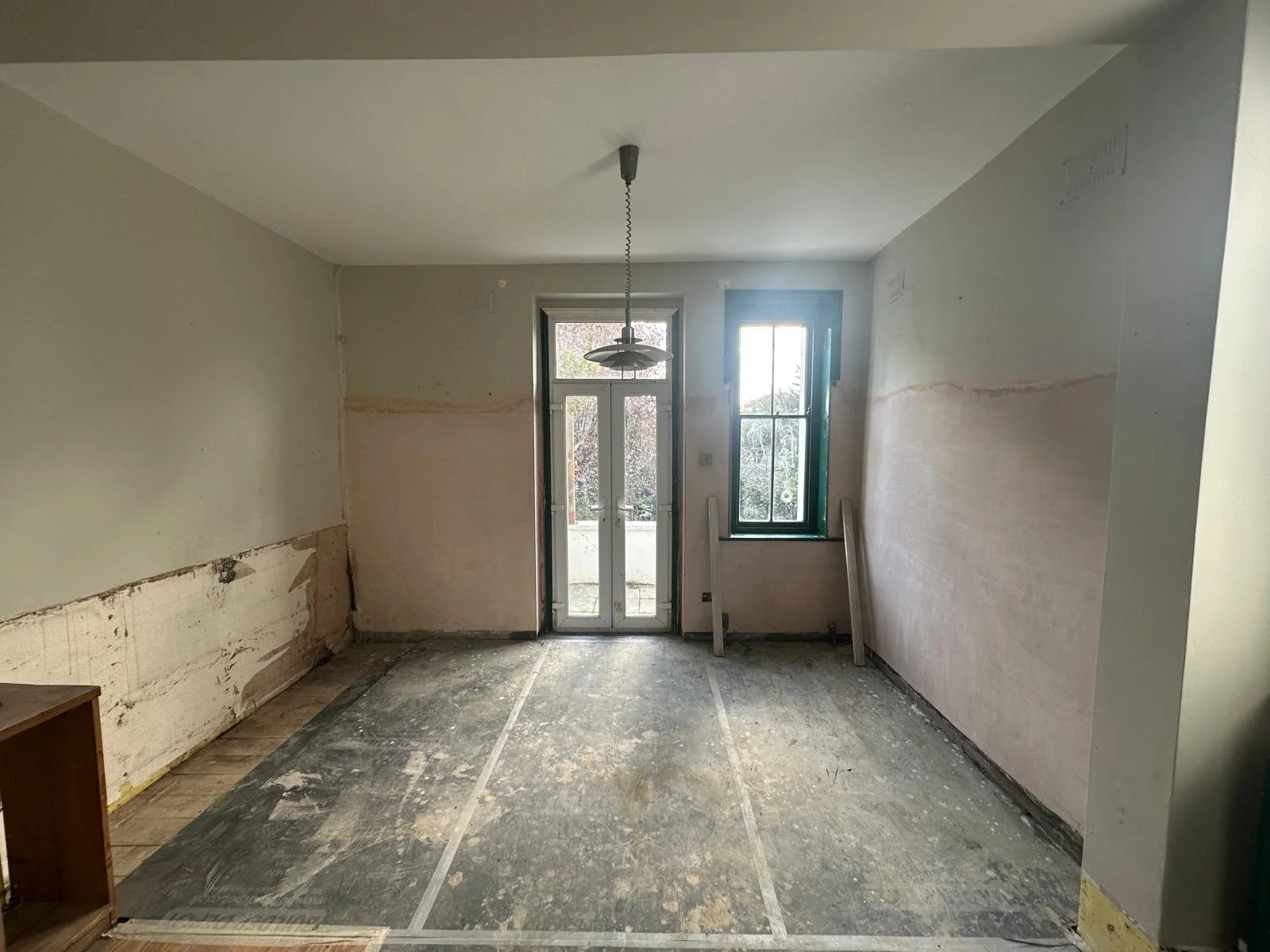 Room under renovation with stripped walls, a doorway with glass, a window, and a pendant light fixture hanging from the ceiling.