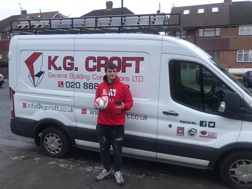 Kevin Croft's son holding a volleyball and a small red object, standing in front of a white van with 'K.G. CROFT General Building Contractors LTD' branding, parked on a residential street.