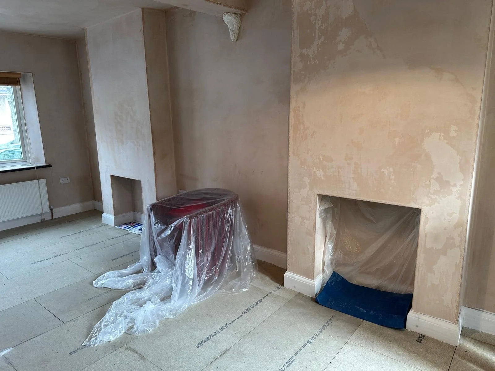 Empty room with partially painted walls, fireplace openings, and a window with a radiator.