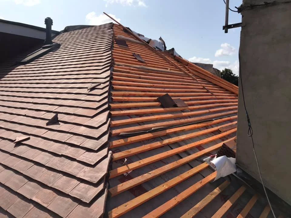 Roof under construction by K G Croft in north london with some tiles removed and wooden rafters exposed, on a house during daylight.