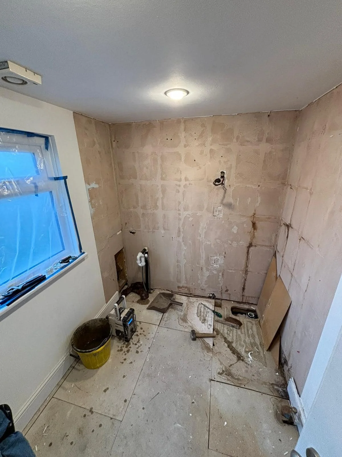 A room in the process of renovation with bare walls, construction tools, and a window covered in plastic.