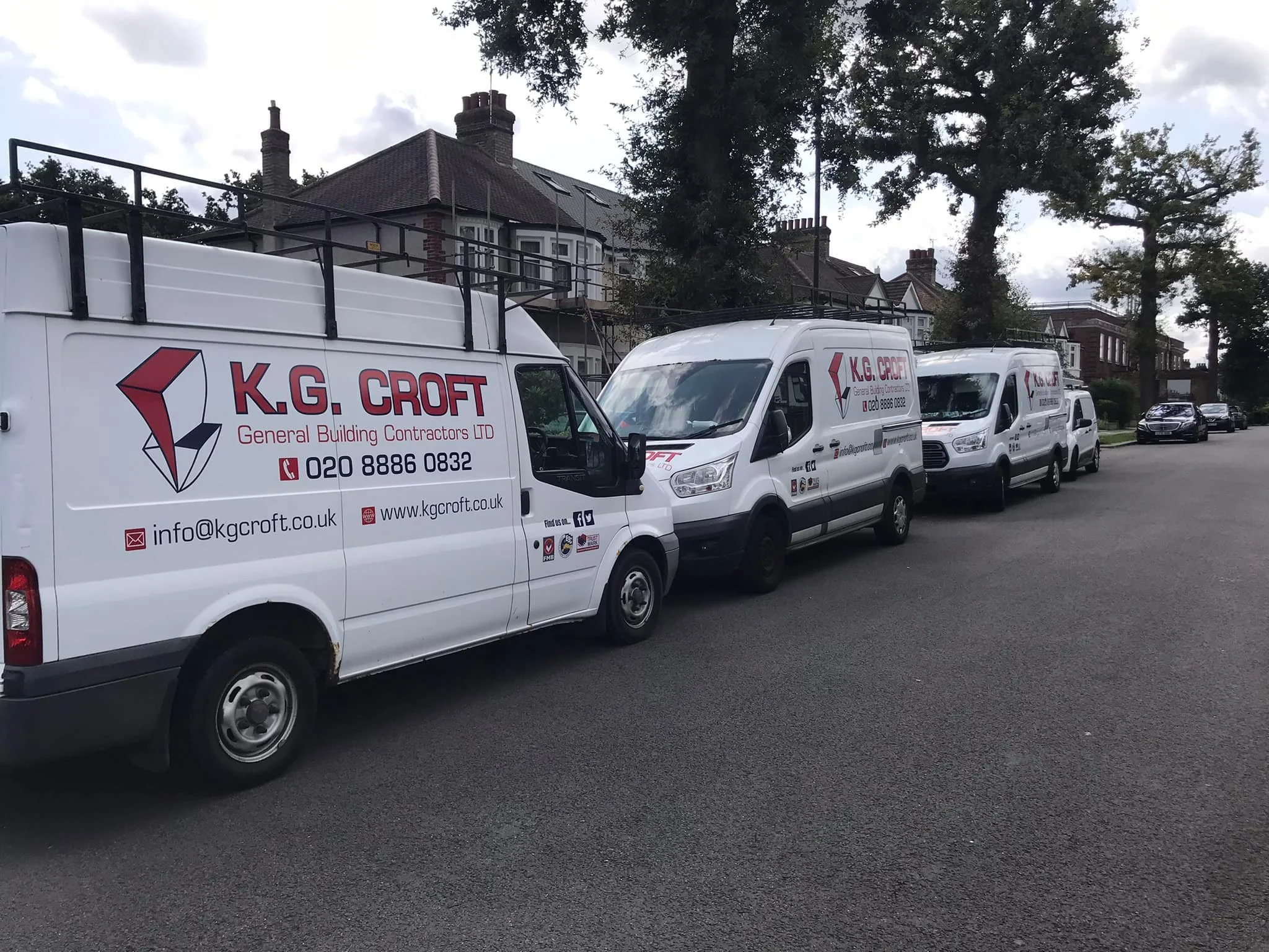 A row of white company vans parked on a residential street in North London, with the logo and contact information for K.G. Croft General Building Contractors LTD on the sides.