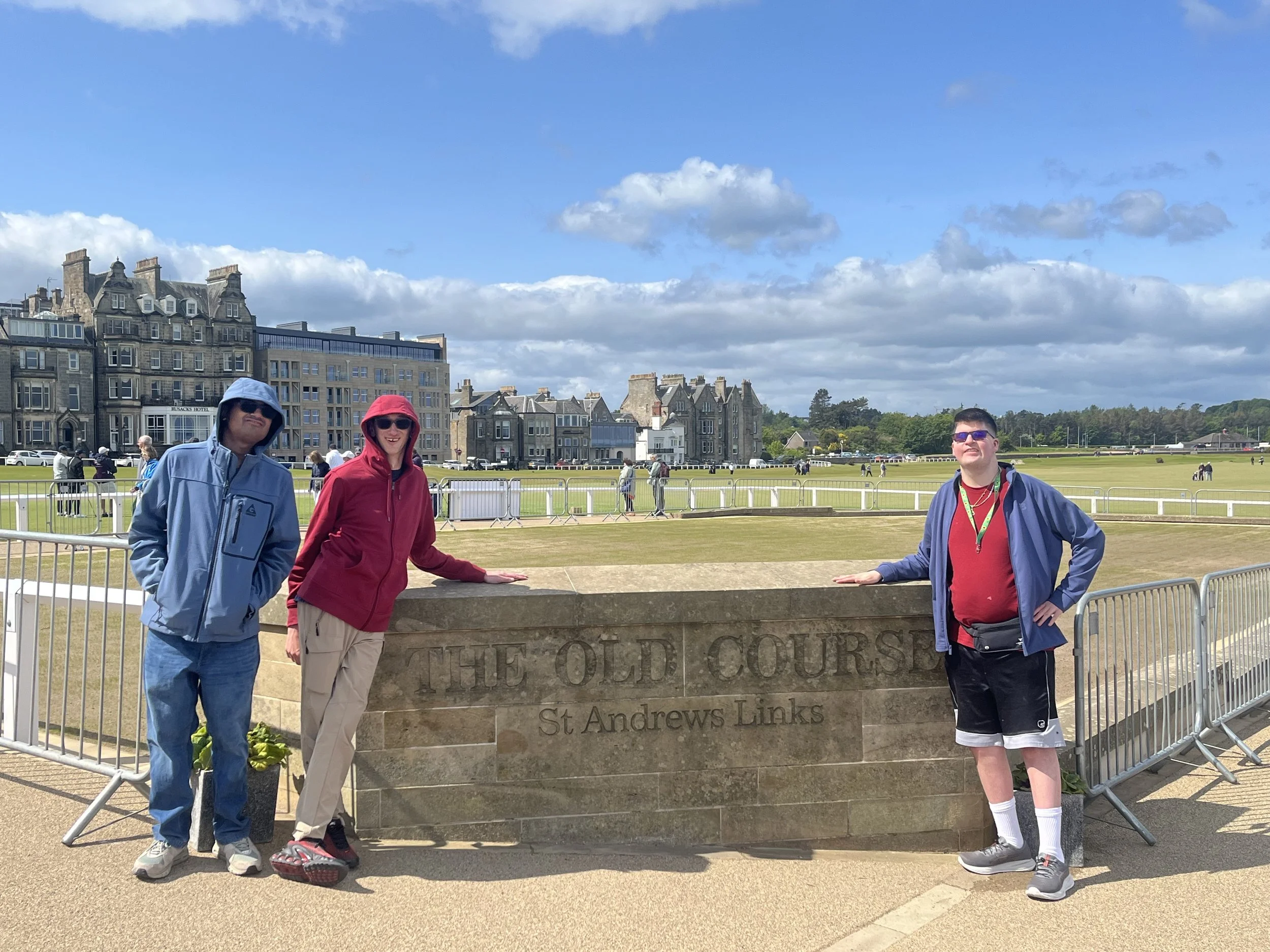 Three men, standing next to sign that says "the old course". Two on the left, wearing red and blue sweater, and one on the right wearing a blue jacket. All are smiling at the camera