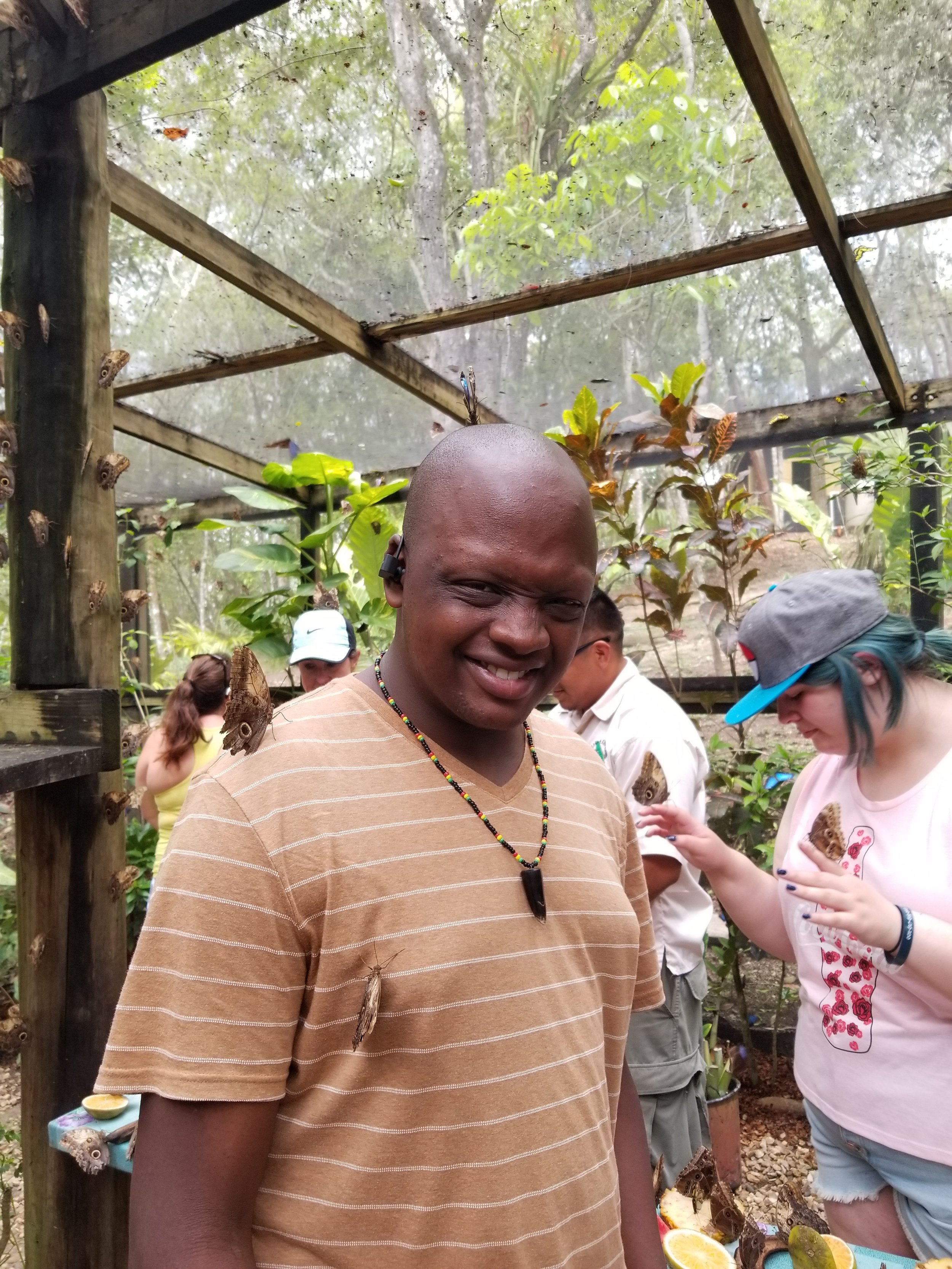 Young man smiles at the camera with a butterfly on his back. 