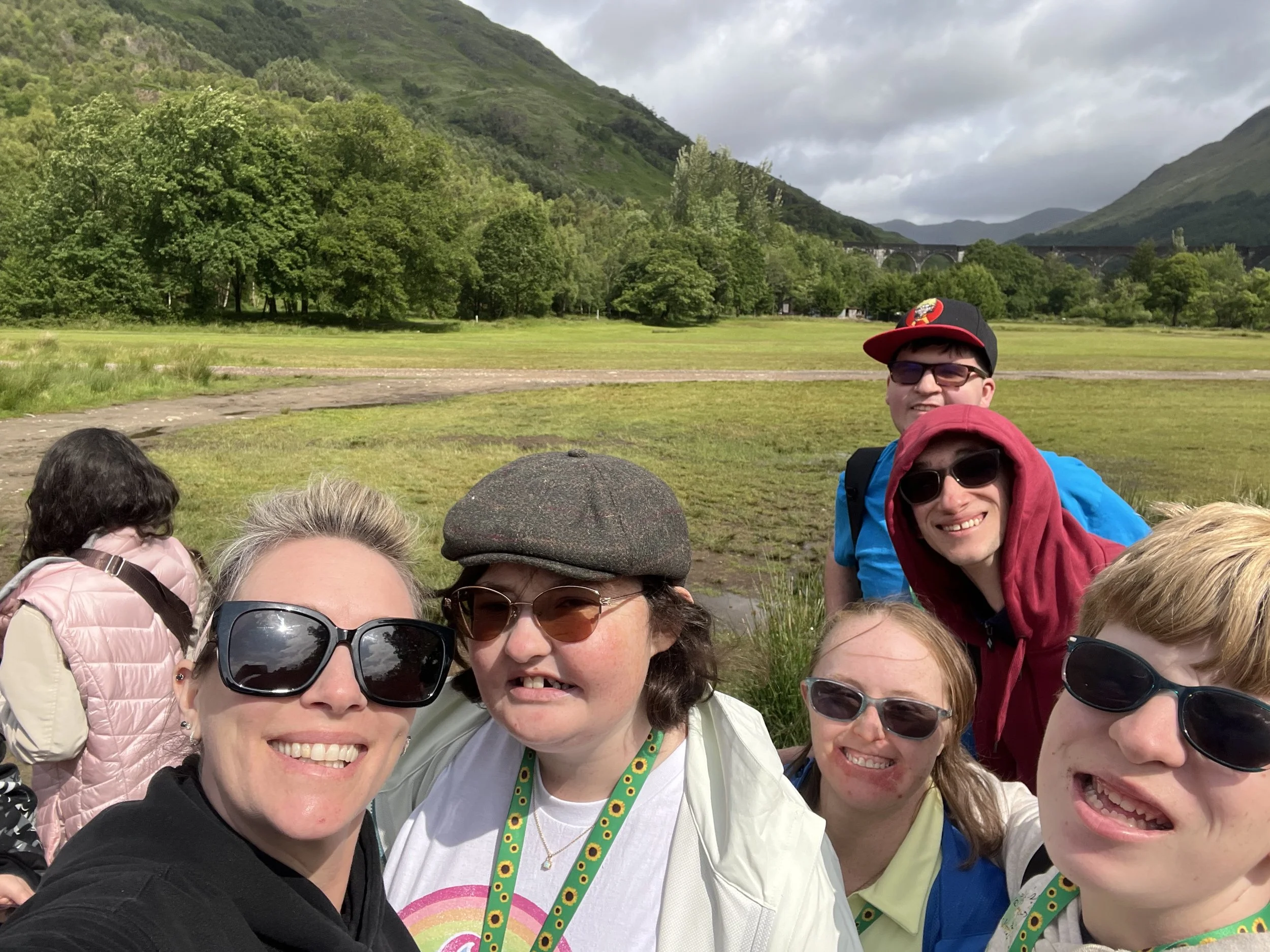 Group smiles at the camera in sunglasses. Behind them is the at the Harry Potter Train line iconic for being in the famous for the scenes of going to Hogwarts. 