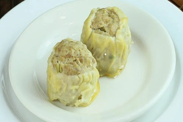 Two meat-filled dumplings topped with yellow dough on a white plate.