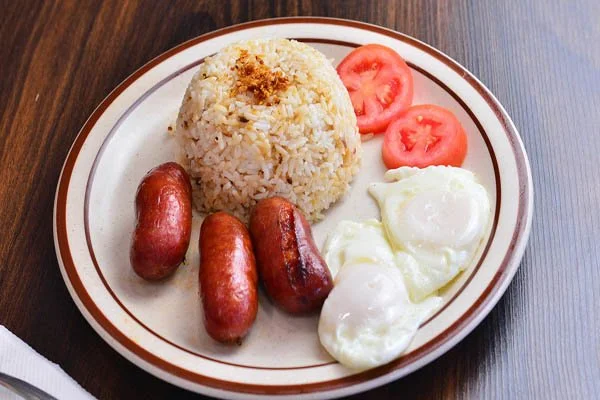 Fried rice with sausage, sliced tomatoes, and fried eggs on a white plate with brown trim.