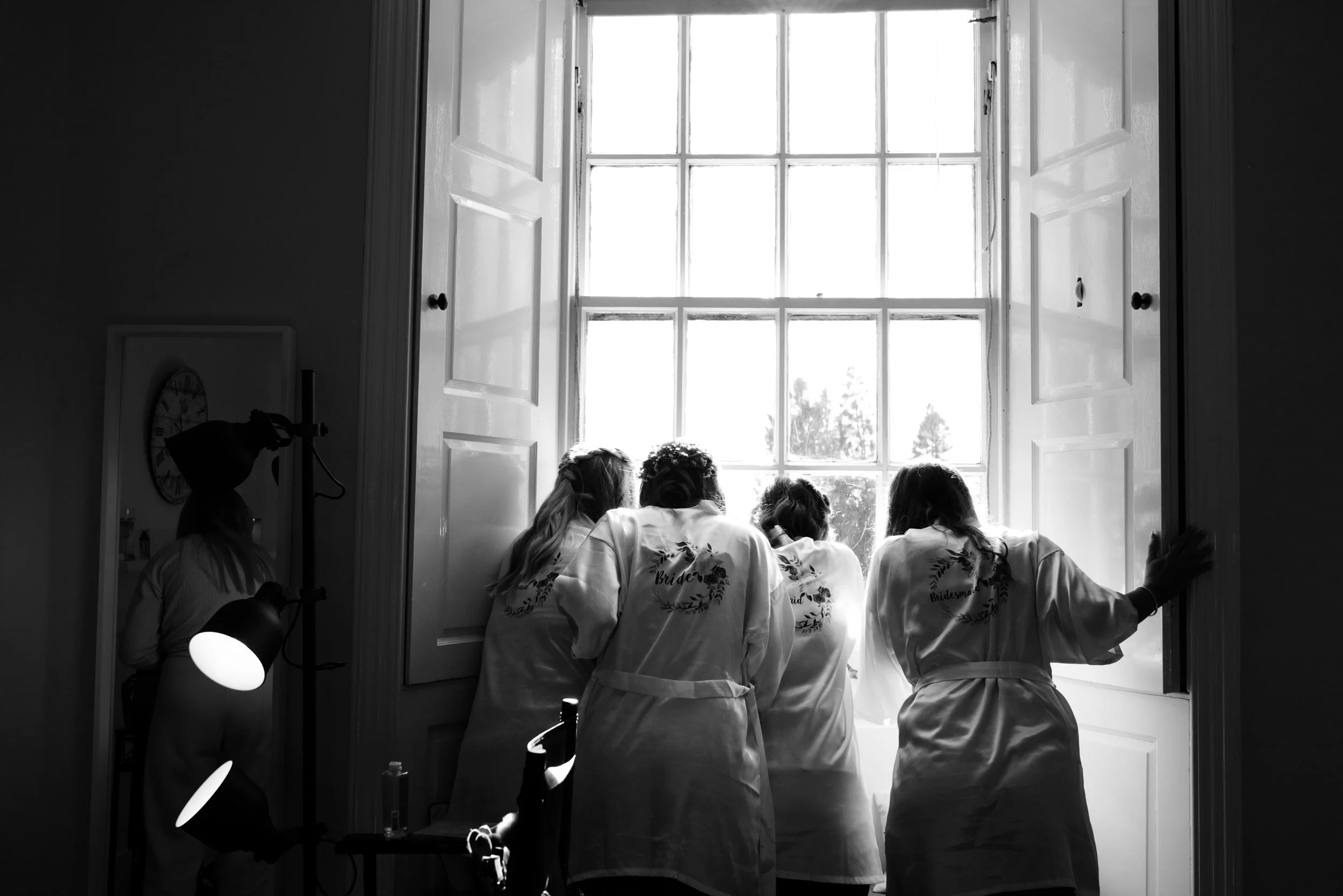 Group of women in robes looking out a large window, possibly part of a wedding preparation.