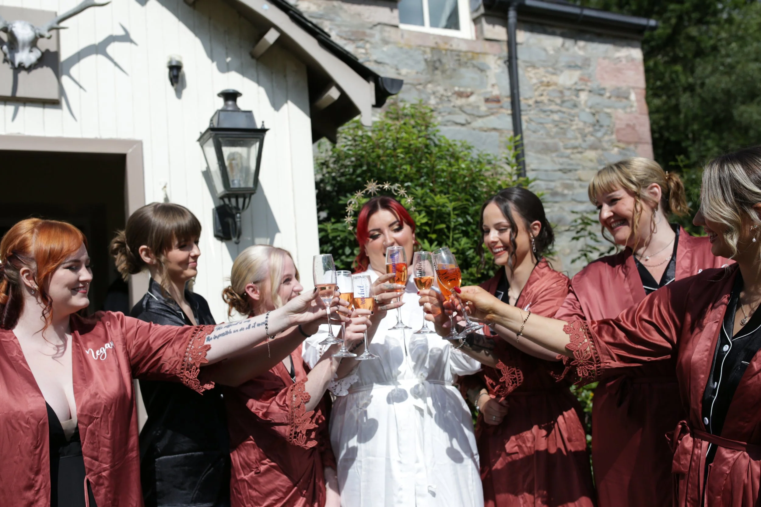 Group of women in wedding robes celebrating with glasses of pink champagne outside a house