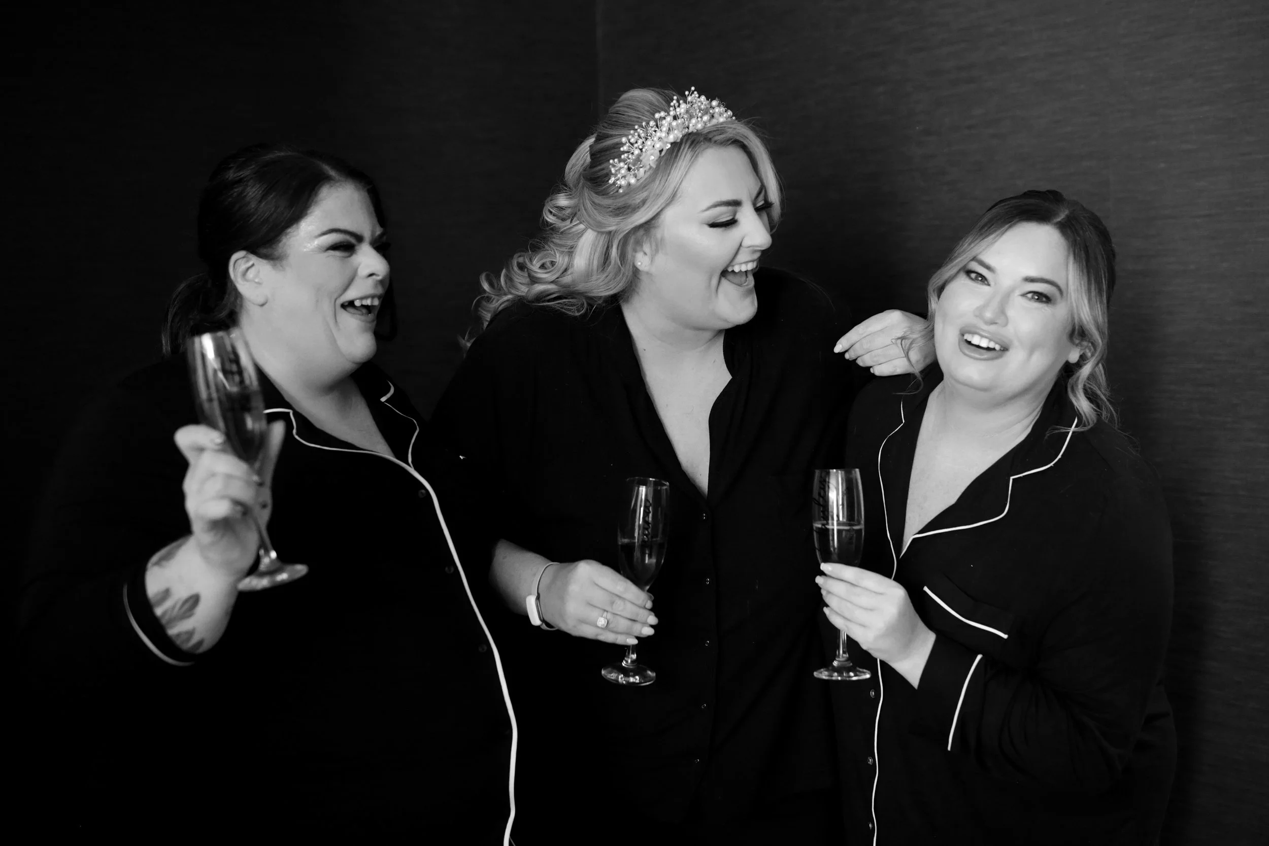 Three women in pajamas celebrating with champagne, smiling and laughing together. bridesmaids, wedding morning.Wedding photography Scotland, Wedding Venue Scotland. 