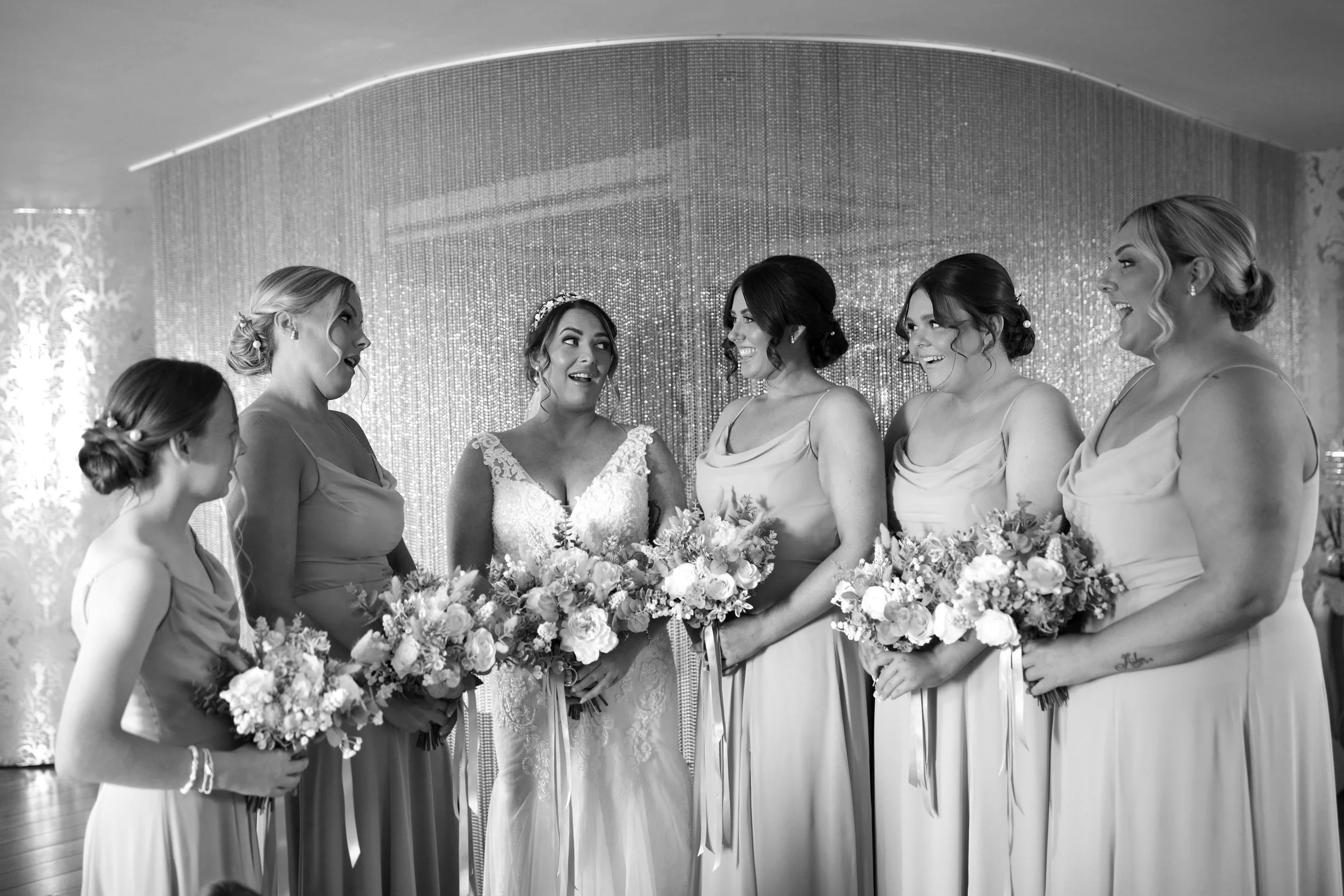 A bride and five bridesmaids standing together, holding bouquets of flowers, at a wedding. Glenskirlie House. Wedding photography Scotland, Wedding Venue Scotland. 