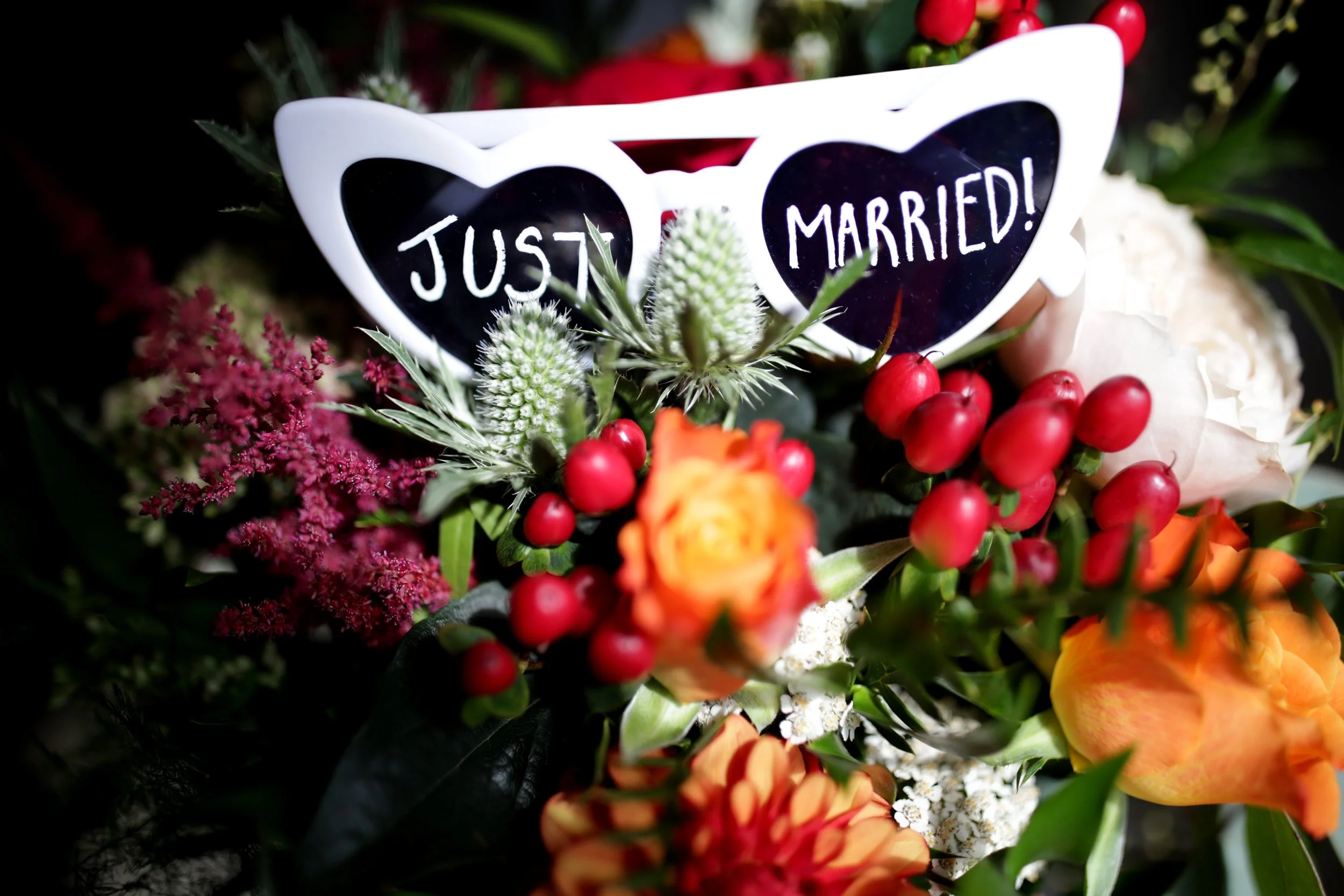 A bouquet of flowers with red berries and eucalyptus, with a white heart-shaped sign reading "Just Married!" in black and white.