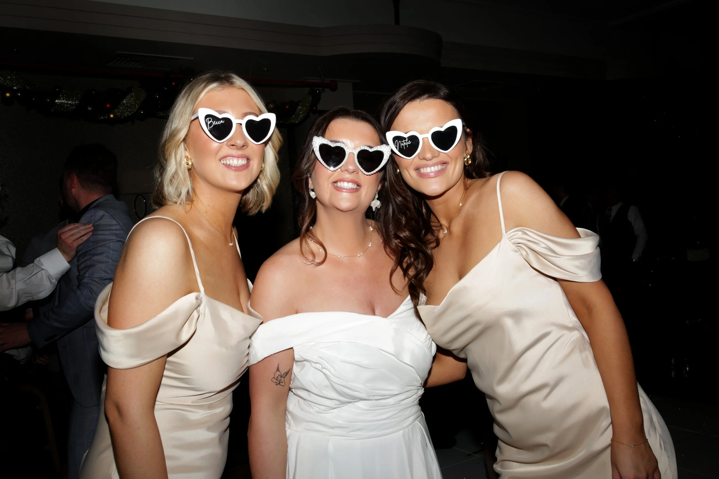 Three women in white dresses wearing heart-shaped sunglasses at a wedding or celebration, smiling and posing for the camera  Wedding photography Scotland, Wedding Venue Scotland. 
