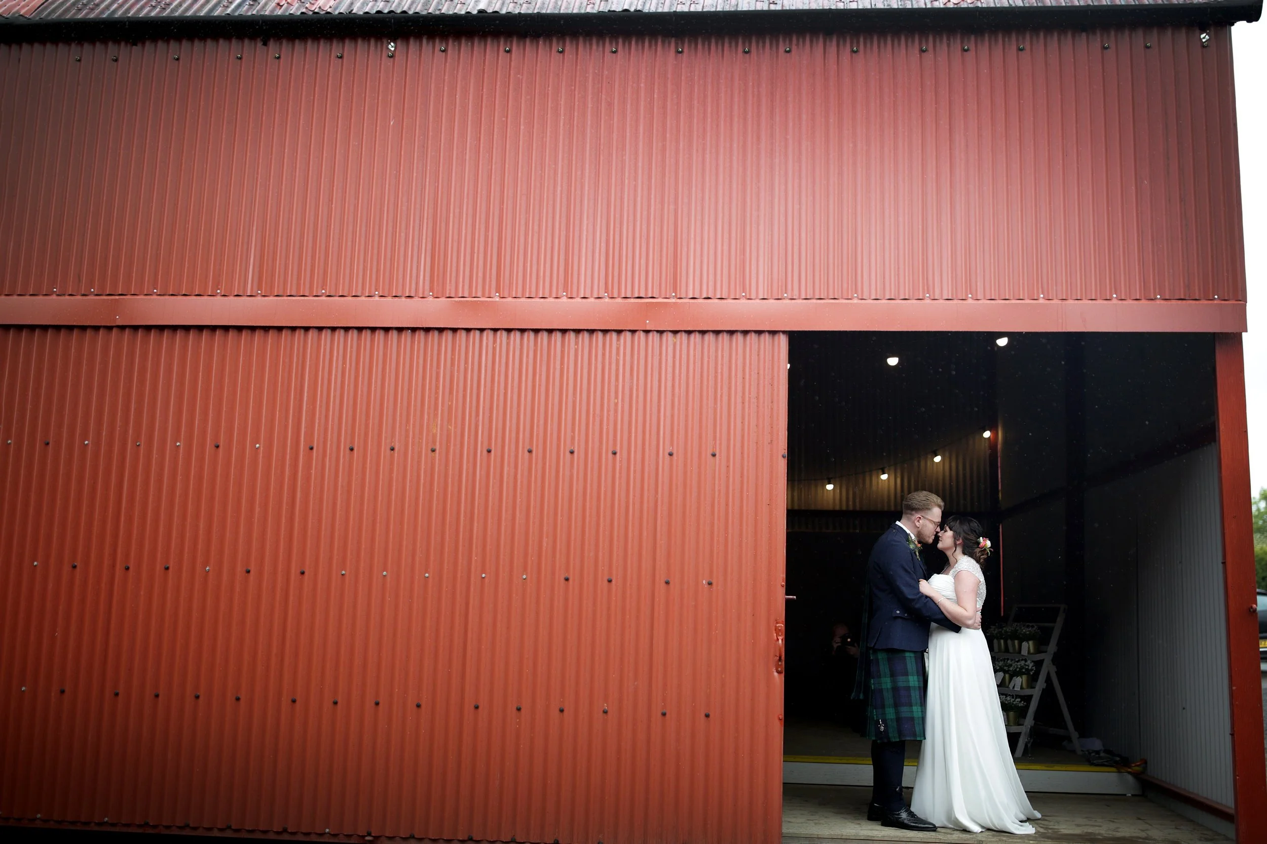 A bride and groom kissing inside a rustic red metal building.