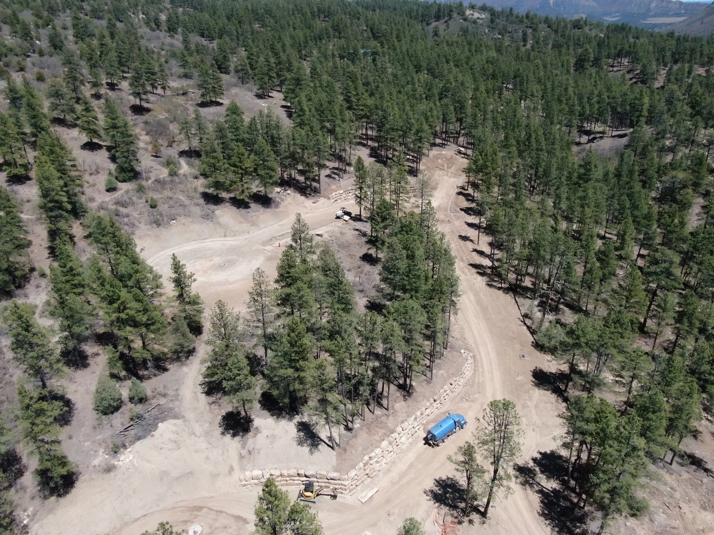 Aerial view of a forested area with a dirt road winding through the trees, construction vehicles, and cleared land.