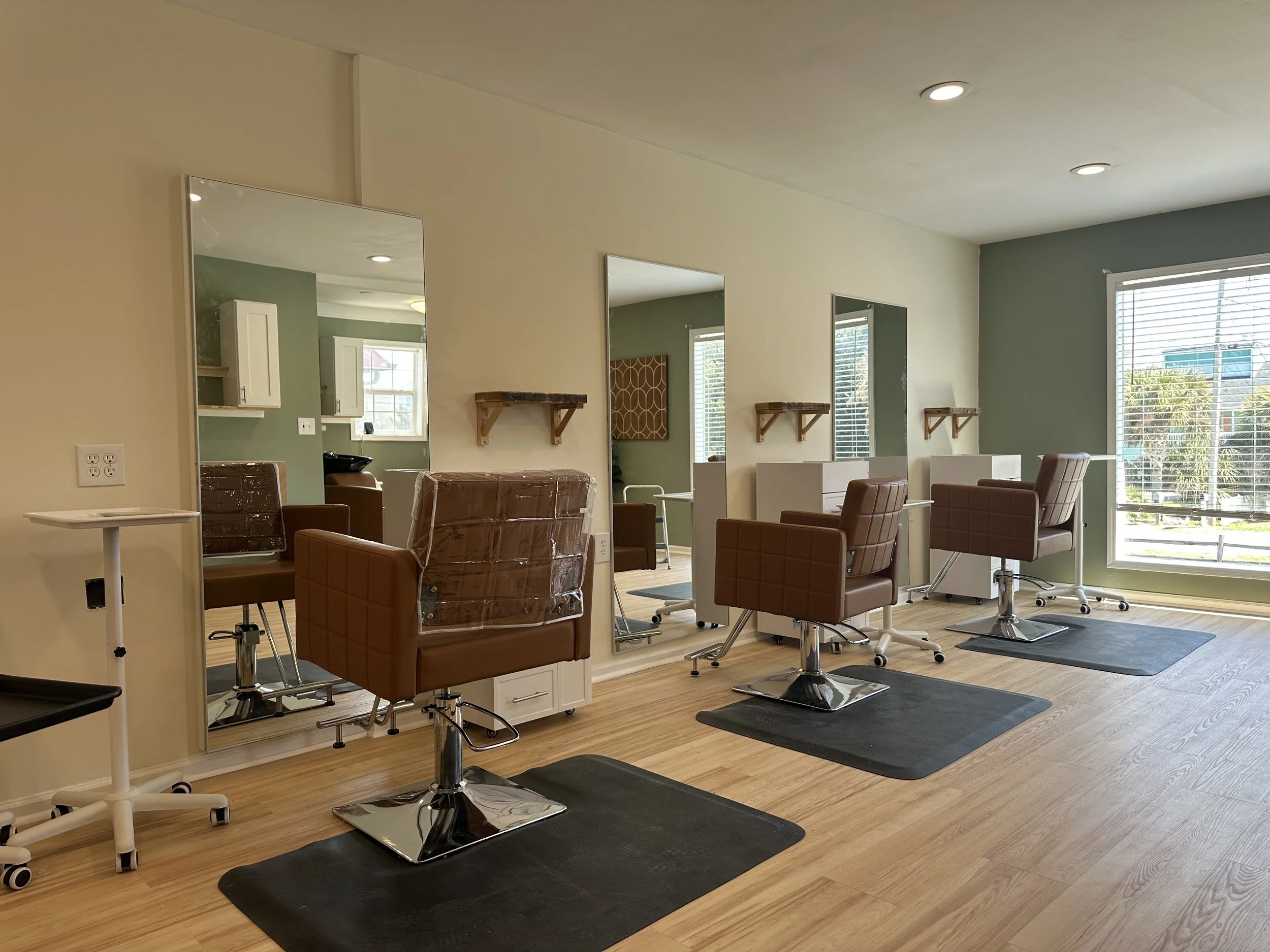 Empty salon with three styling chairs, large mirrors, and a large window with blinds.